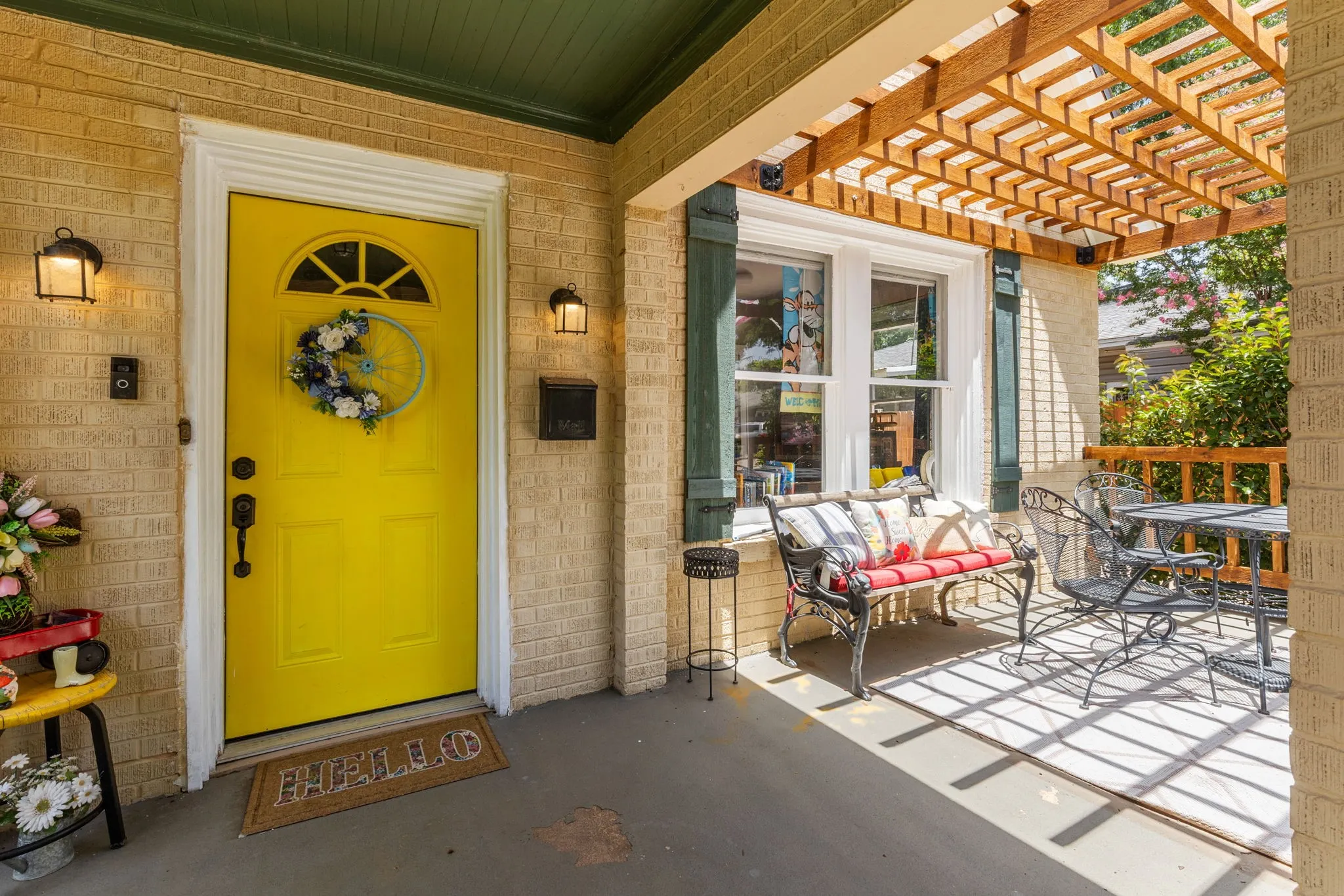 Inviting front porch featuring a vibrant yellow entry, flanked by two outdoor wall lanterns. Brand new pergola just completed.