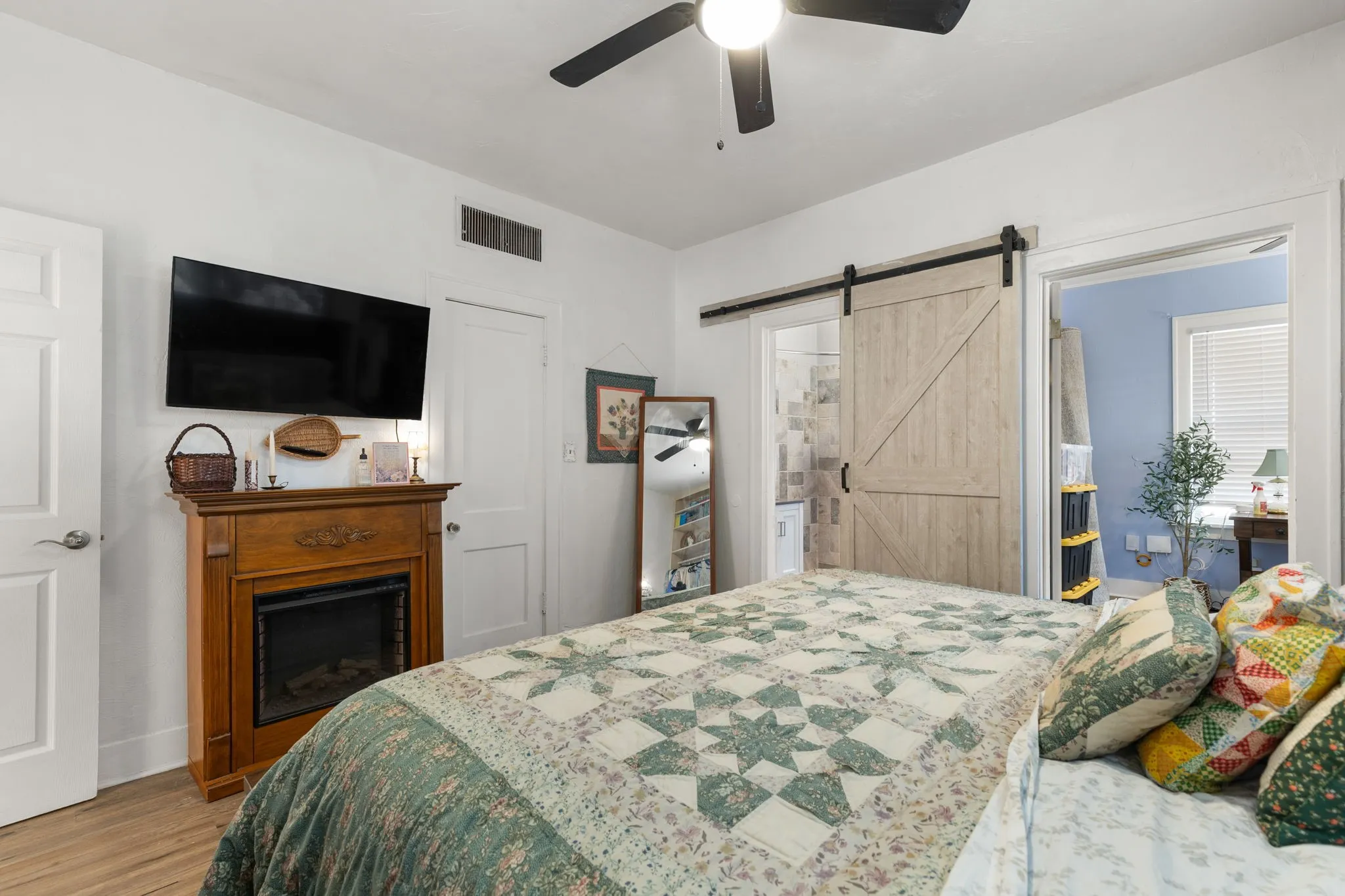 Primary bedroom featuring a wood-like faux fireplace, black ceiling fan and barn door to the bathroom