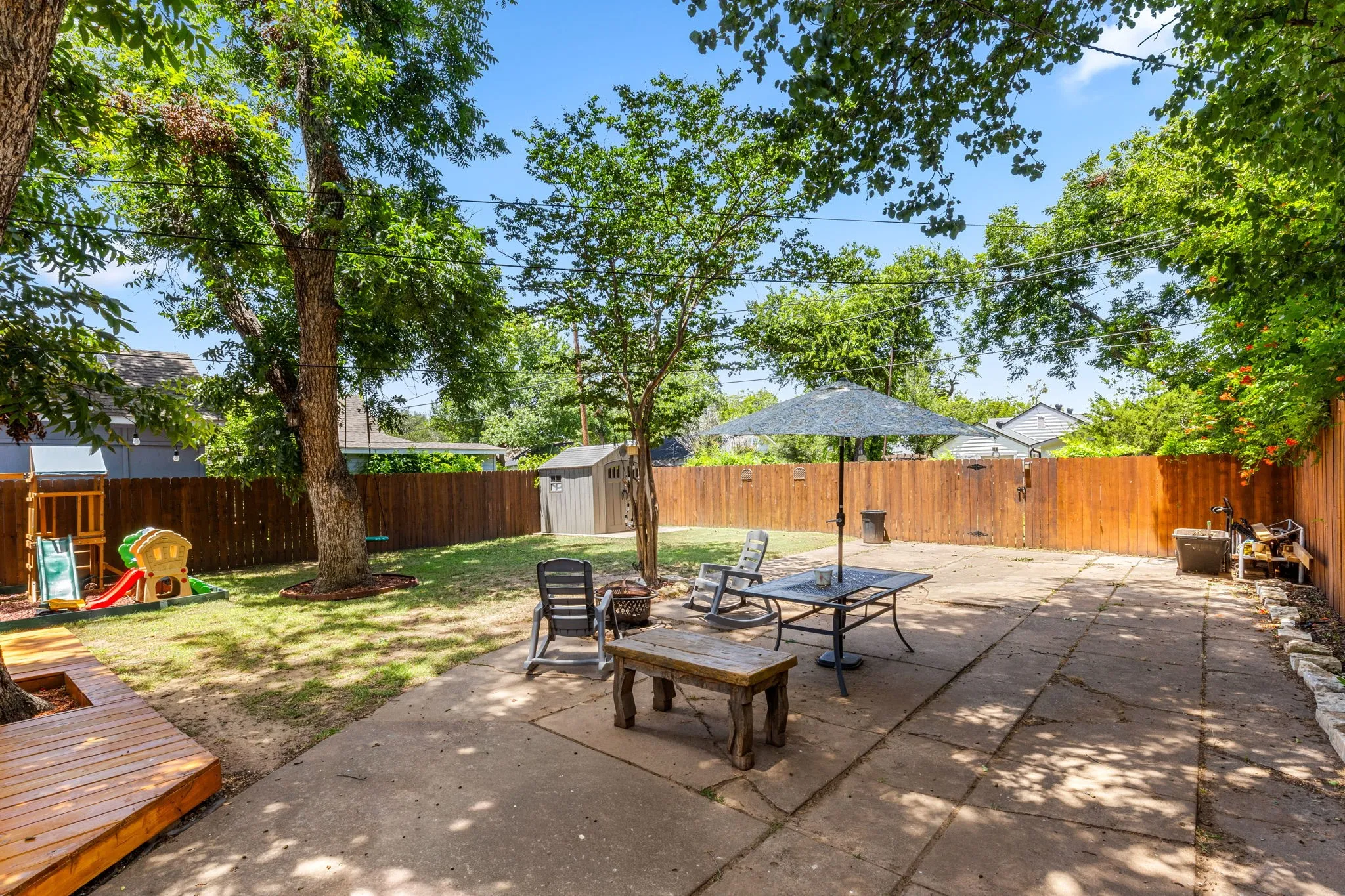 Expansive backyard featuring a large concrete patio, manicured lawn, and mature trees