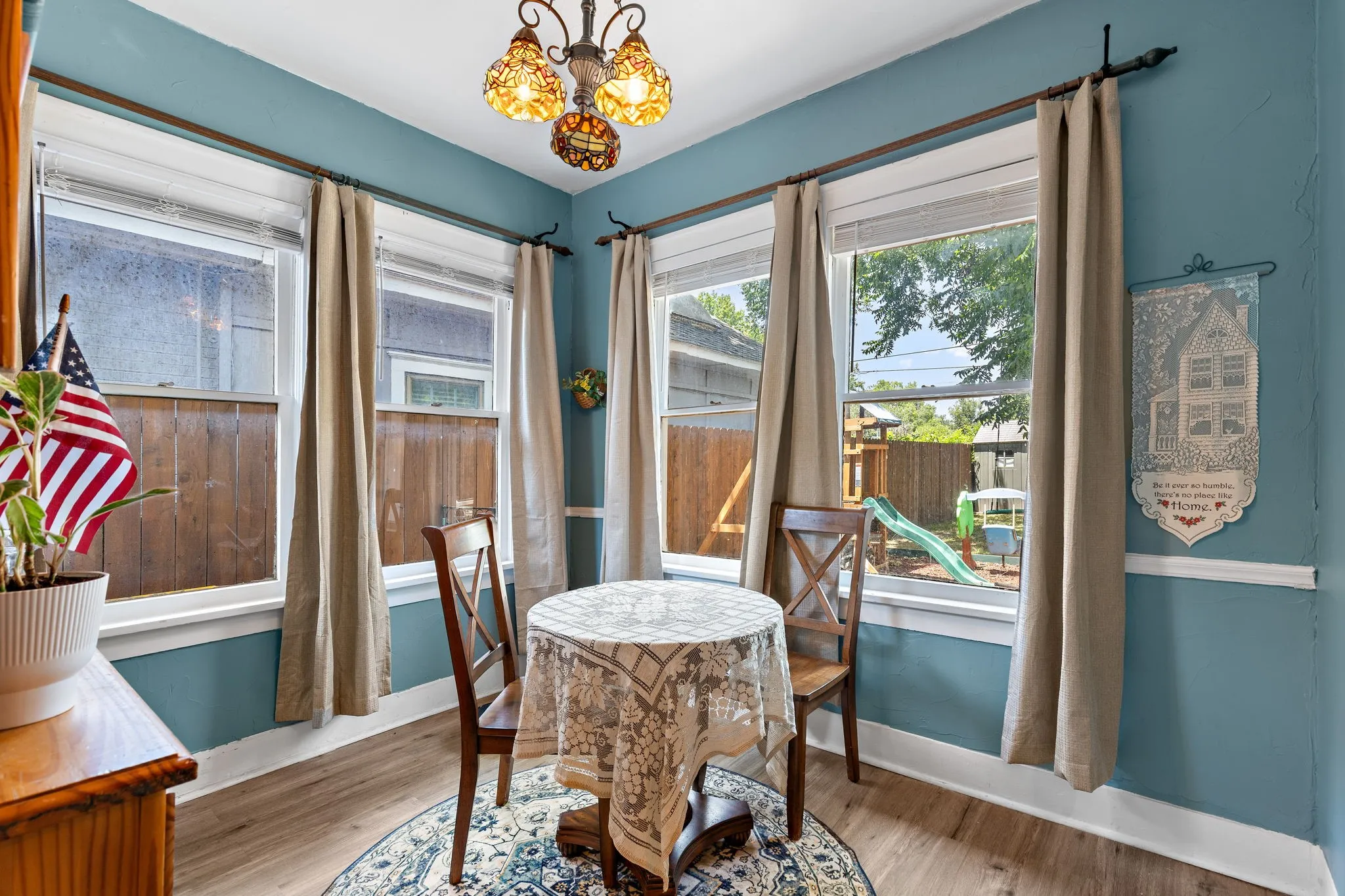 Bright dining area featuring wood-like flooring, a decorative chandelier, and four large windows providing ample natural light