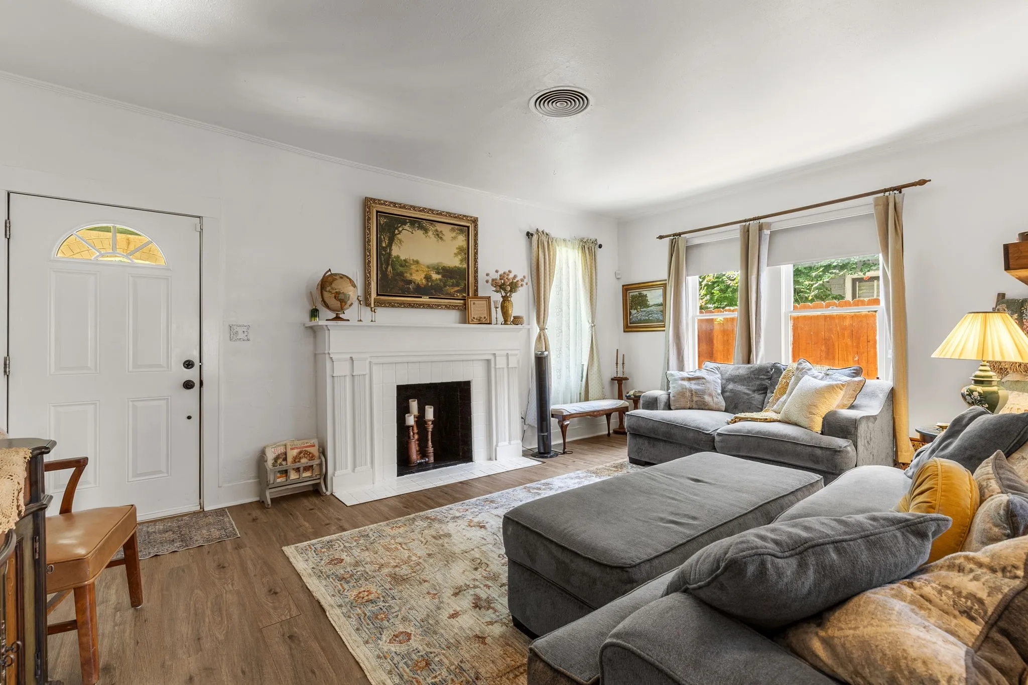 Living area featuring wood-finish flooring, a white paneled entry door with an arched transom, and a classic white fireplace with mantel