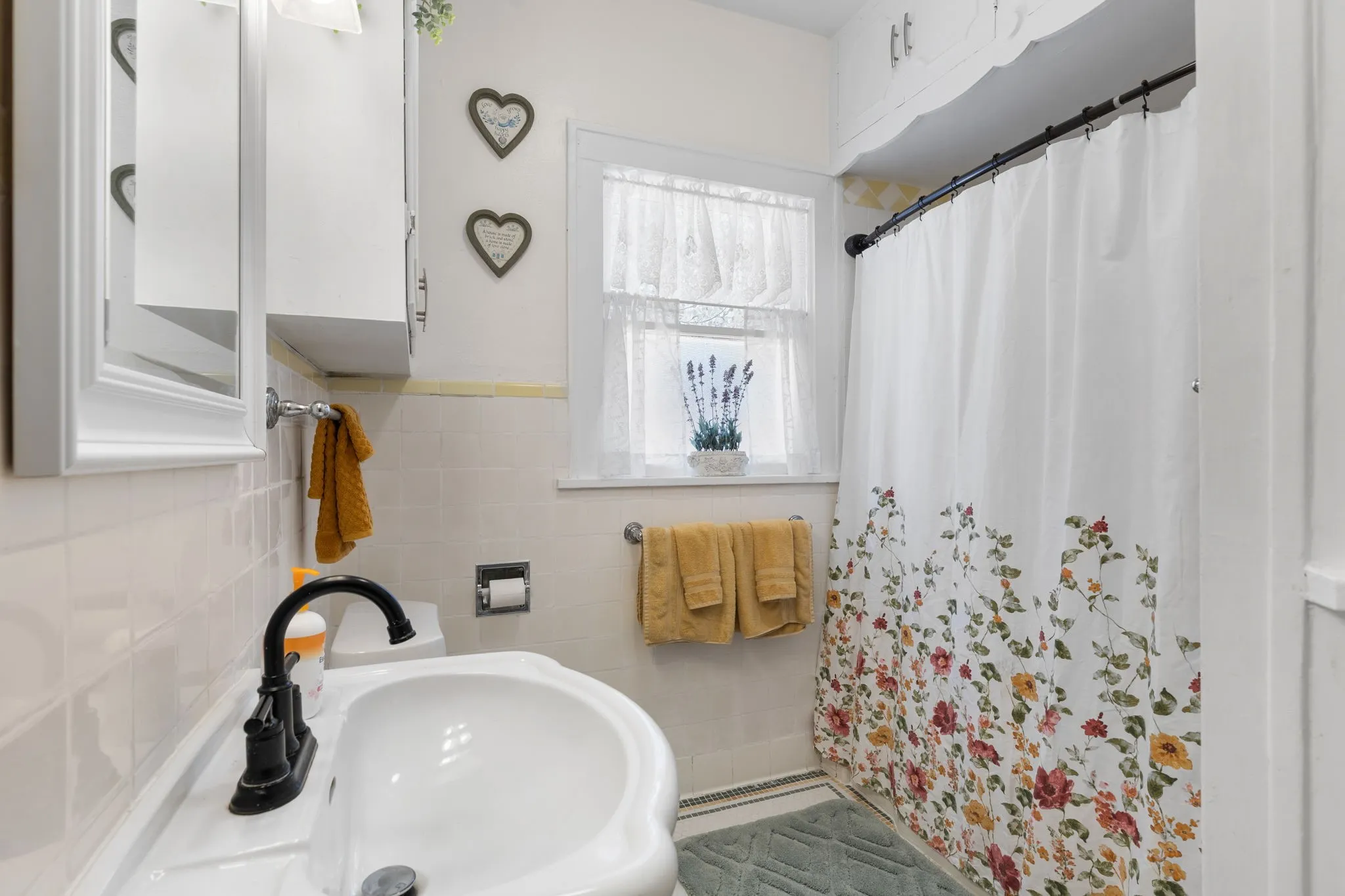 Bathroom featuring a ceramic pedestal sink with a matte black faucet, white tiled walls, and a window with natural light