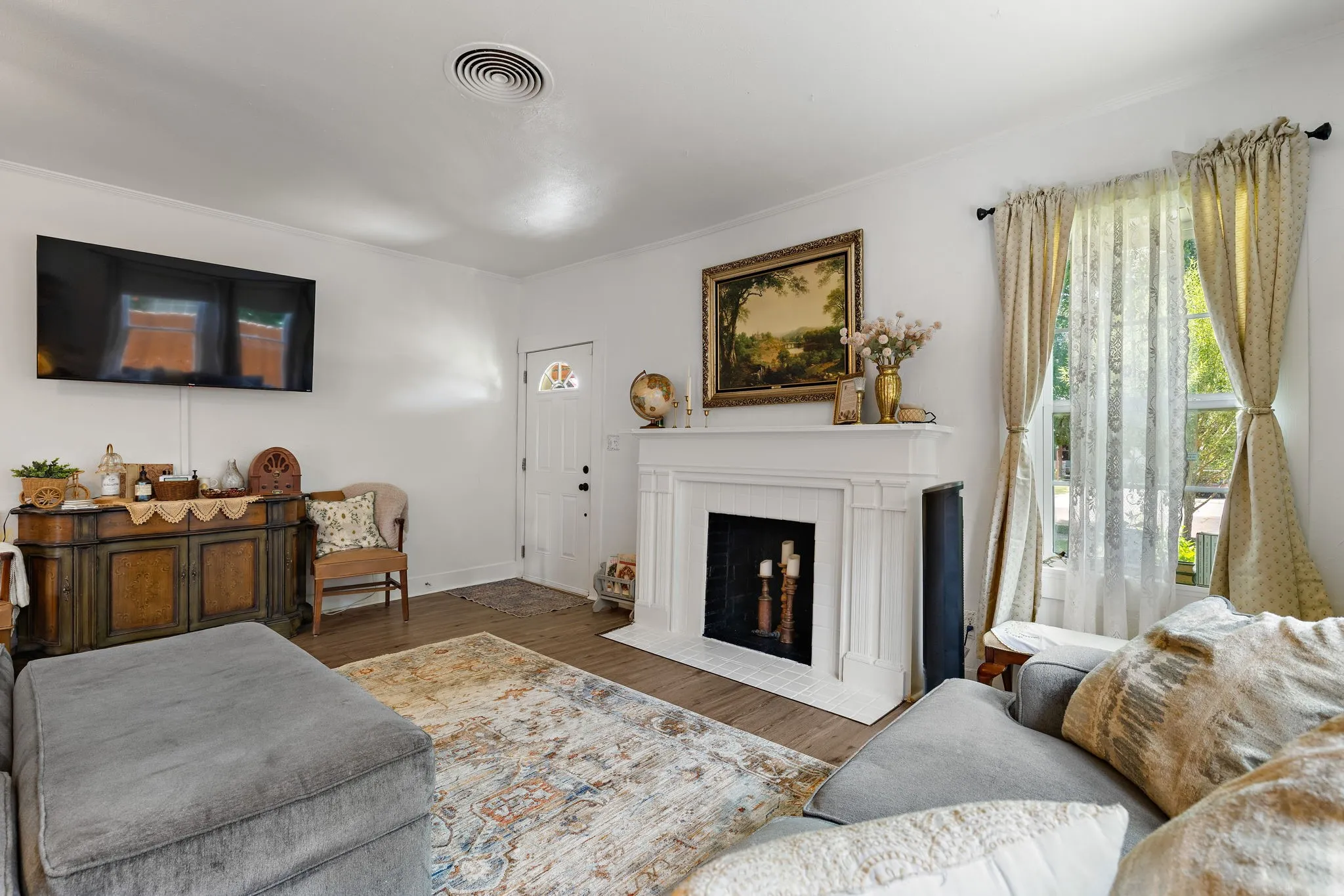 Living area featuring a prominent white mantelpiece, a front entry door with a decorative glass insert, wood-finish flooring, and a large window providing natural light