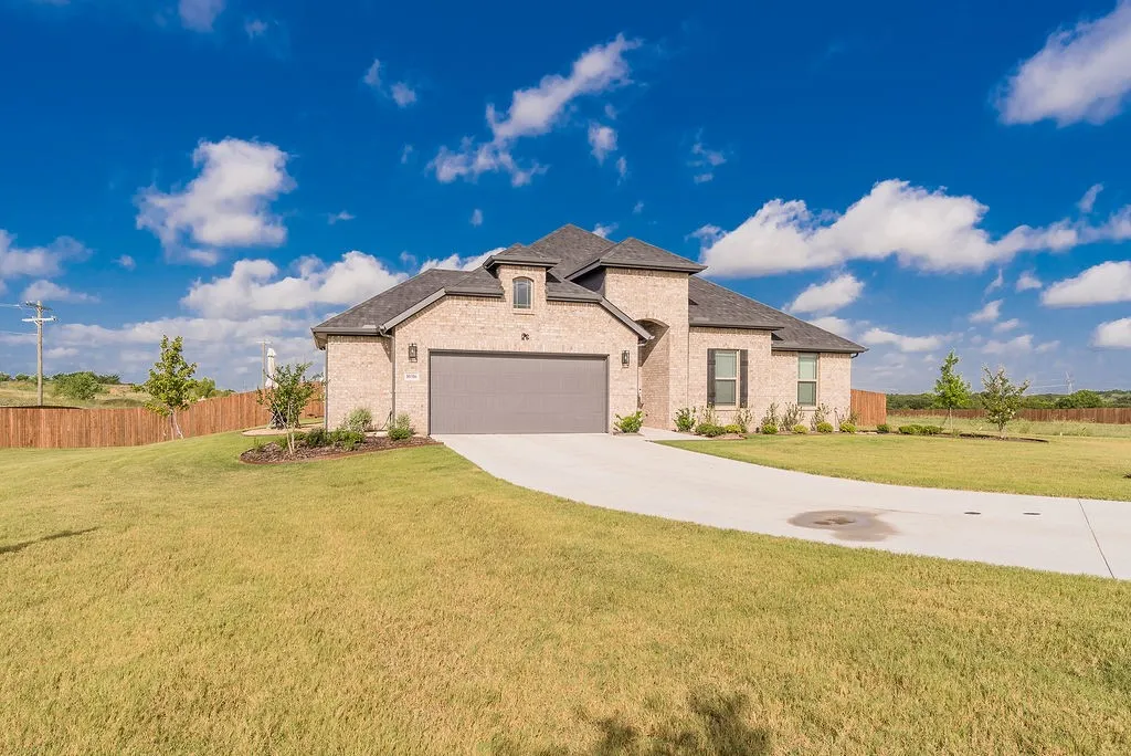 Brick exterior residence with a dark shingle roof, arched entry with a modern door, and a 2.5-car garage