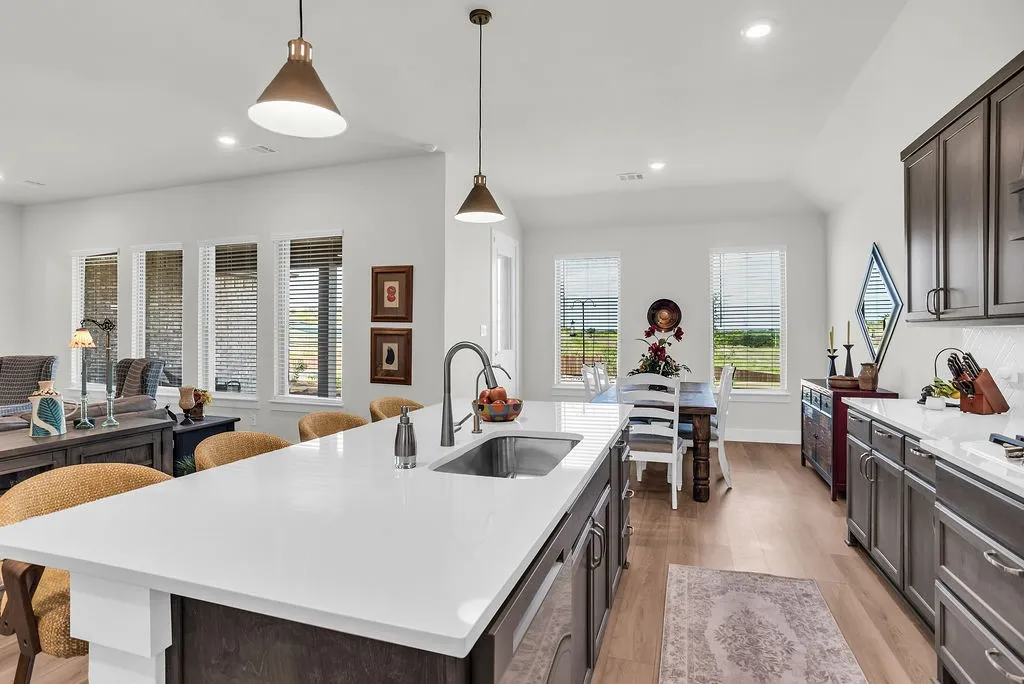 Kitchen featuring a substantial island with breakfast bar, undermount sink with gooseneck brushed nickel faucet, wood-finish flooring, dark wood cabinetry, a white herringbone tile backsplash, walk-in pantry and stainless steel appliances including a propane gas cooktop, electric built-in oven and microwave open to living and breakfast rooms