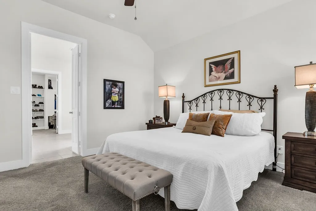 Main bedroom features an ensuite bath, vaulted ceilings, plush carpeting, a ceiling fan with integrated lighting, backyard views, and white walls.