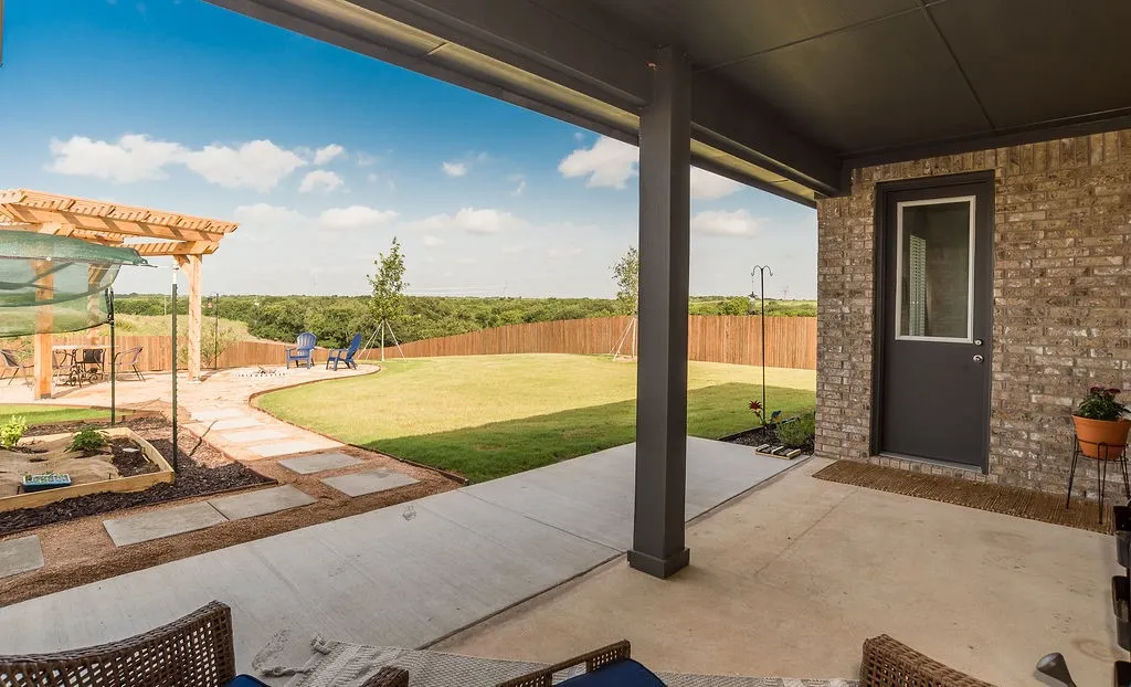Expansive backyard featuring a covered patio extended to a wooden pergola living space, vegetable garden, a large grassy area, and a privacy fence.