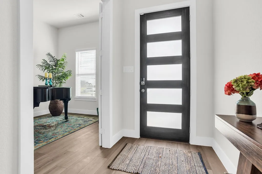 Modern entry door featuring frosted glass insets flooding the room with natural light, wood-finish flooring, and white trim throughout open to the study.