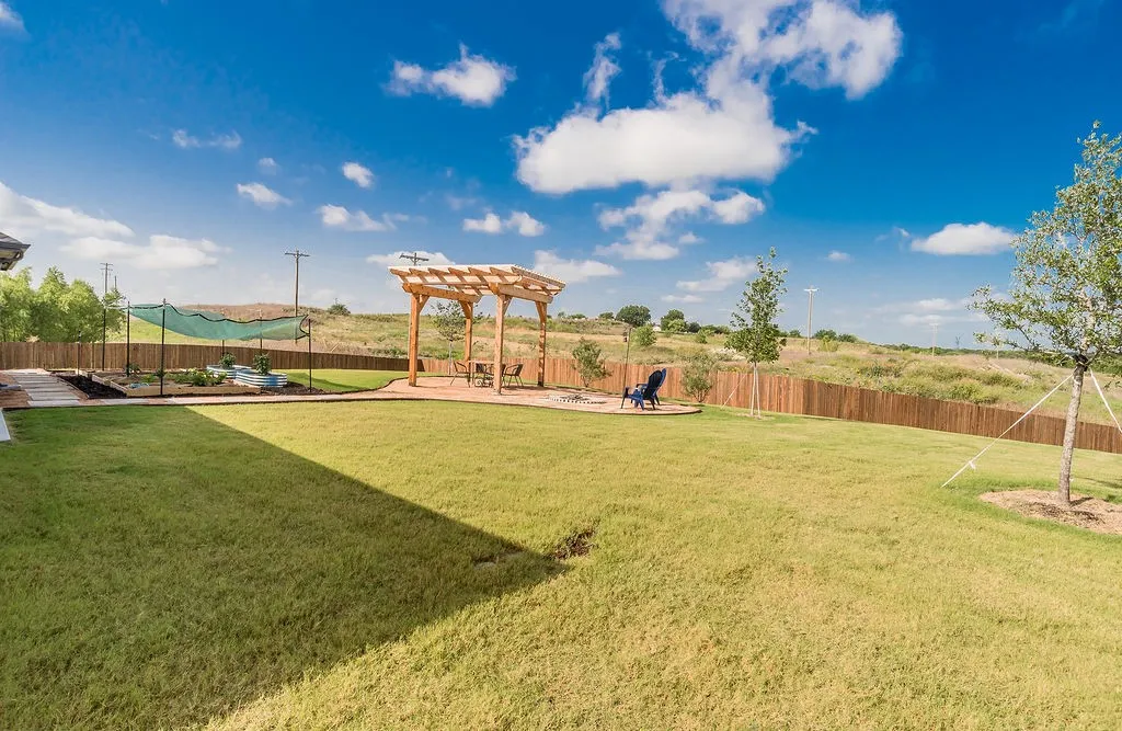 Expansive backyard featuring a large grassy area, a wooden pergola over a patio, and a privacy fence