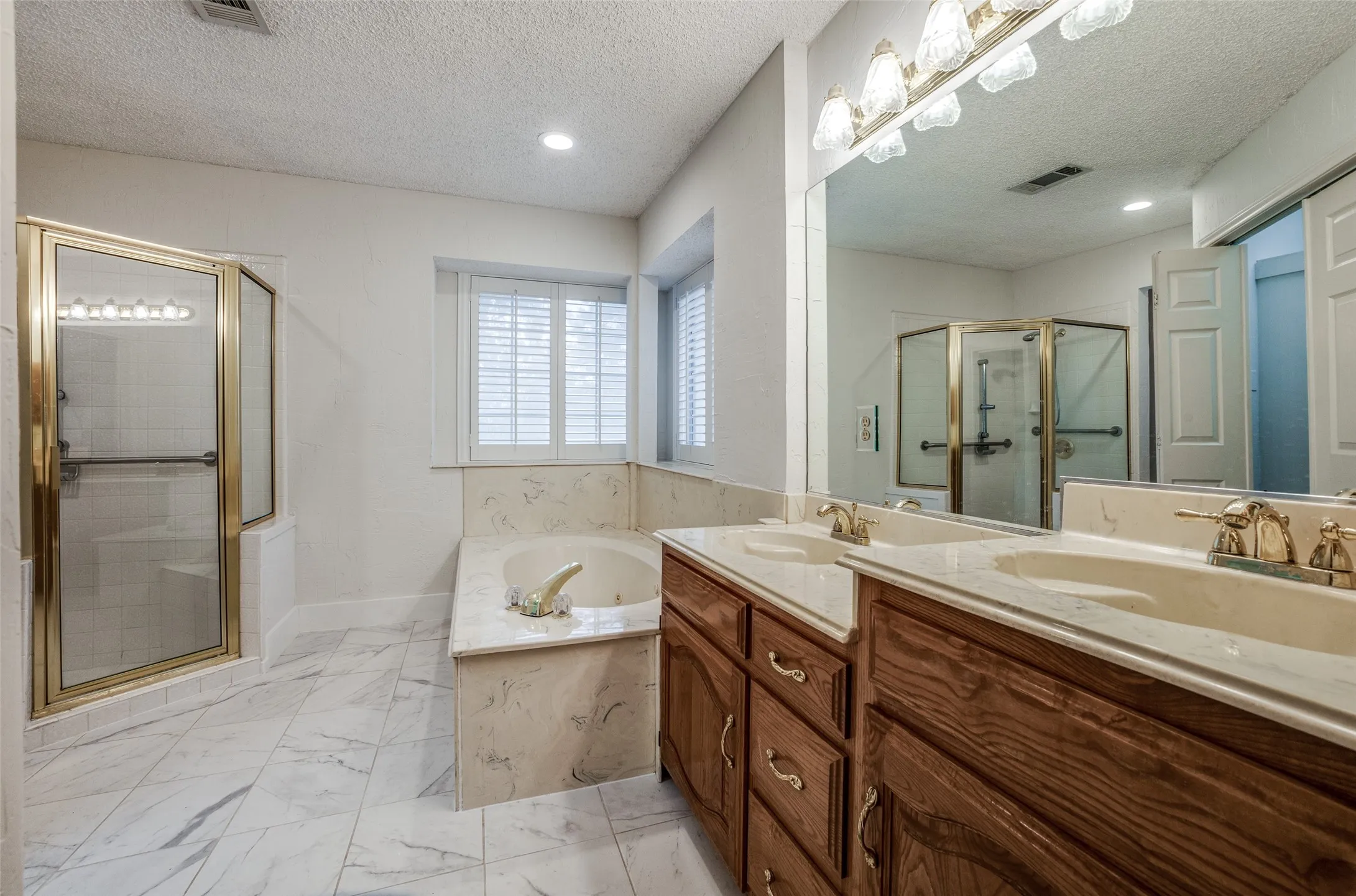 Spacious bathroom featuring a double vanity with wood-finish cabinetry, a large built-in mirror, and a jetted soaking tub