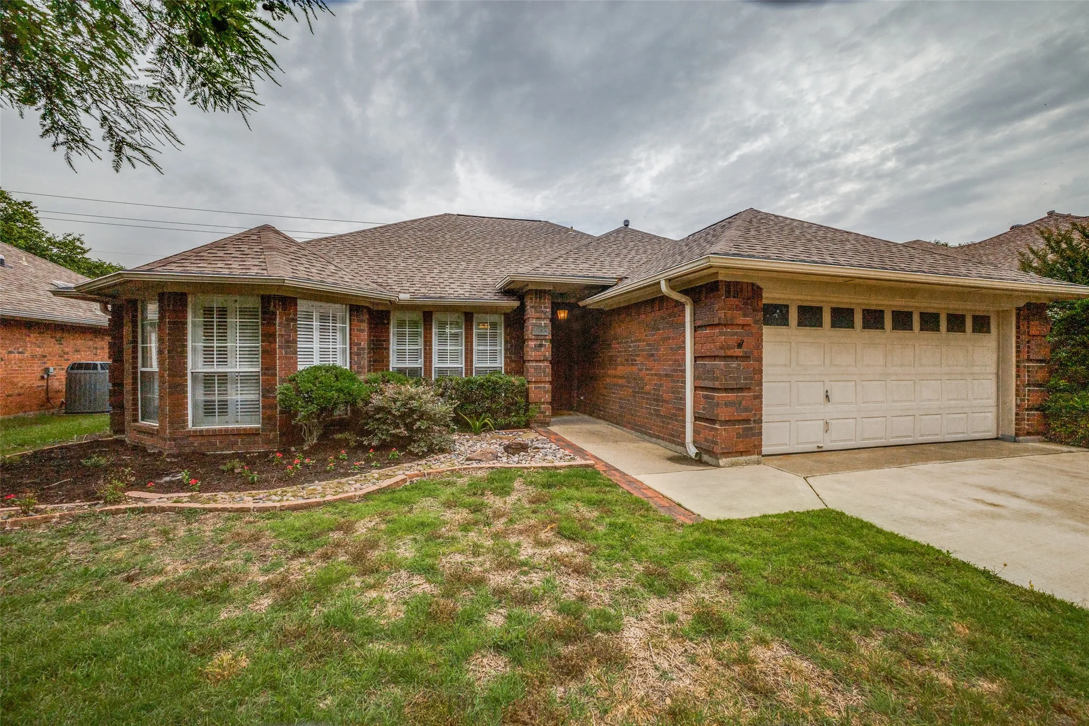 Brick exterior with a traditional architectural style, featuring a two-car garage, bay windows, a gabled roofline, and a concrete driveway