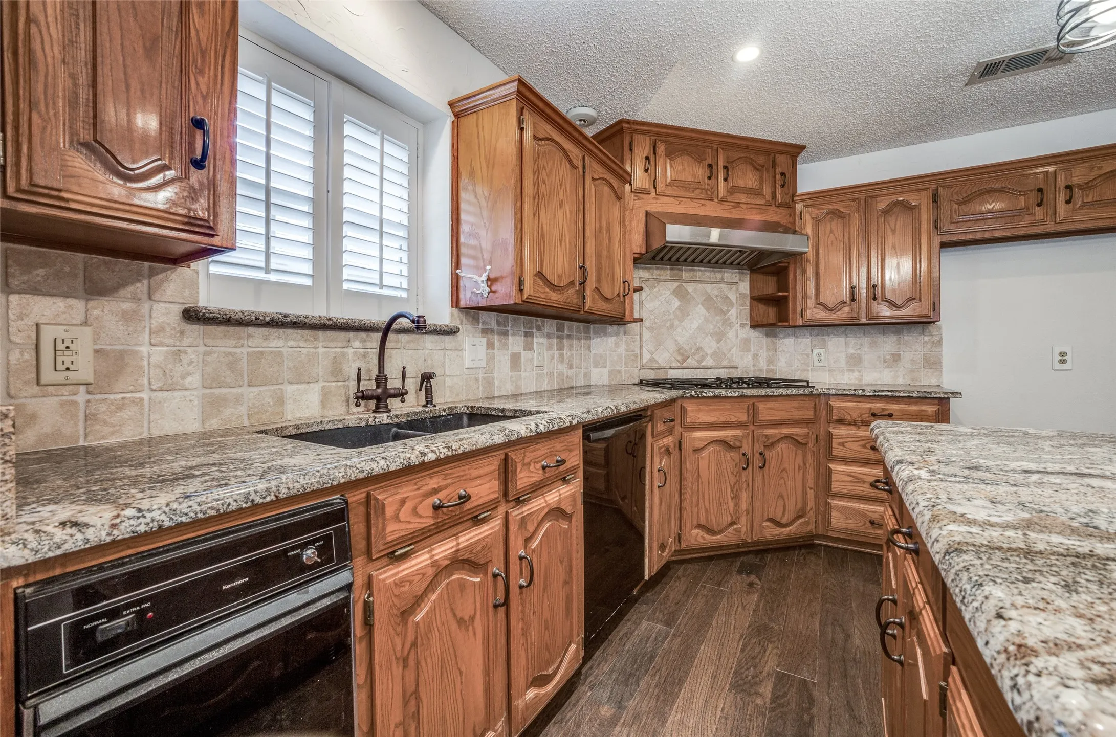 Kitchen featuring wood cabinetry, granite countertops, tile backsplash, wood-finish flooring, and a stainless steel range hood