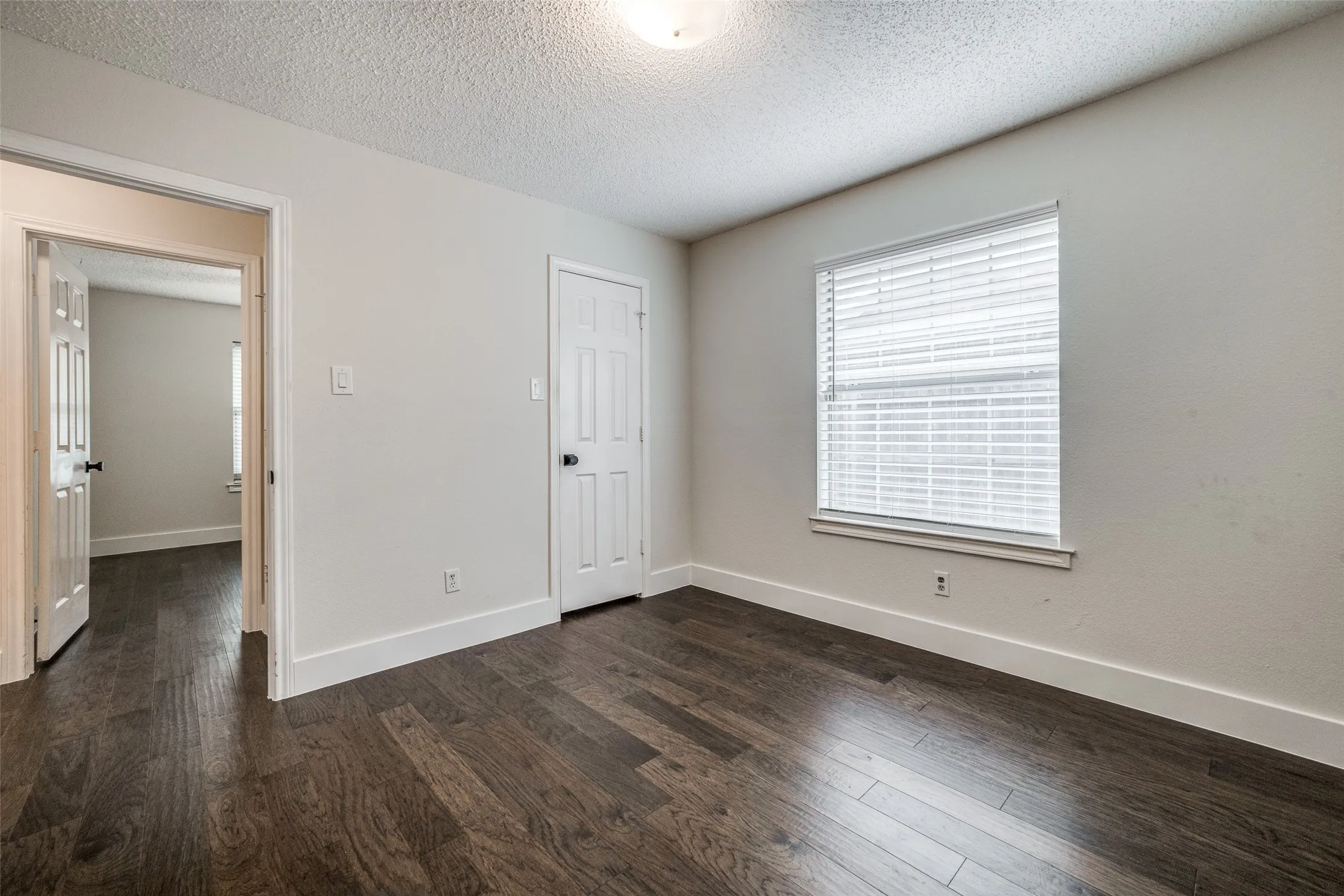 Bright interior space featuring dark wood-finish flooring, white baseboards, and a single window with horizontal blinds