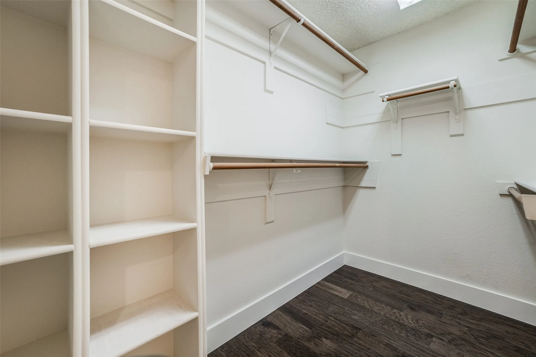 Walk-in closet featuring built-in shelving, multiple hanging rods, white trim, and wood-finish flooring