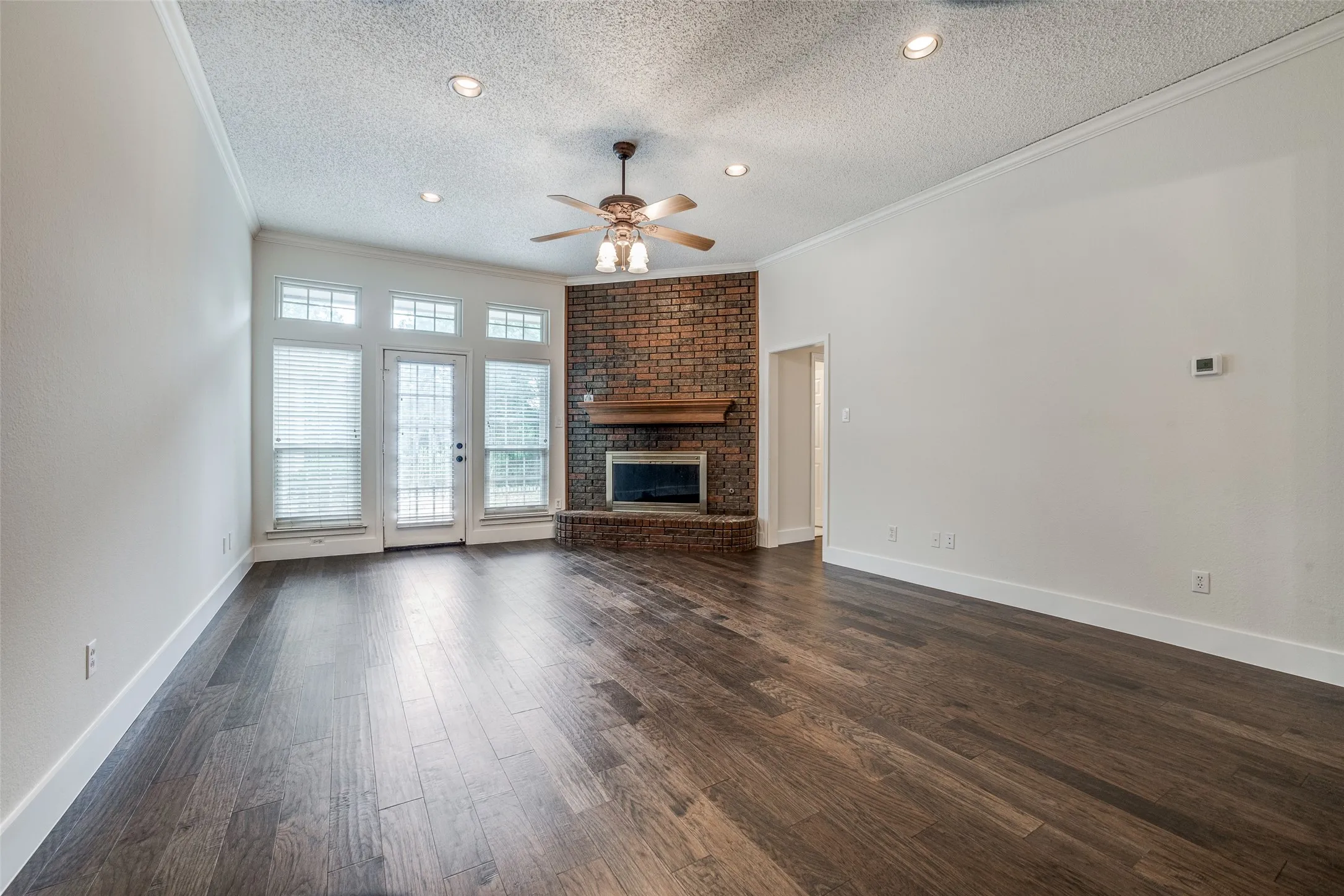 Living area featuring wood-finish flooring, a brick fireplace with a wood mantel, and multiple windows with transoms