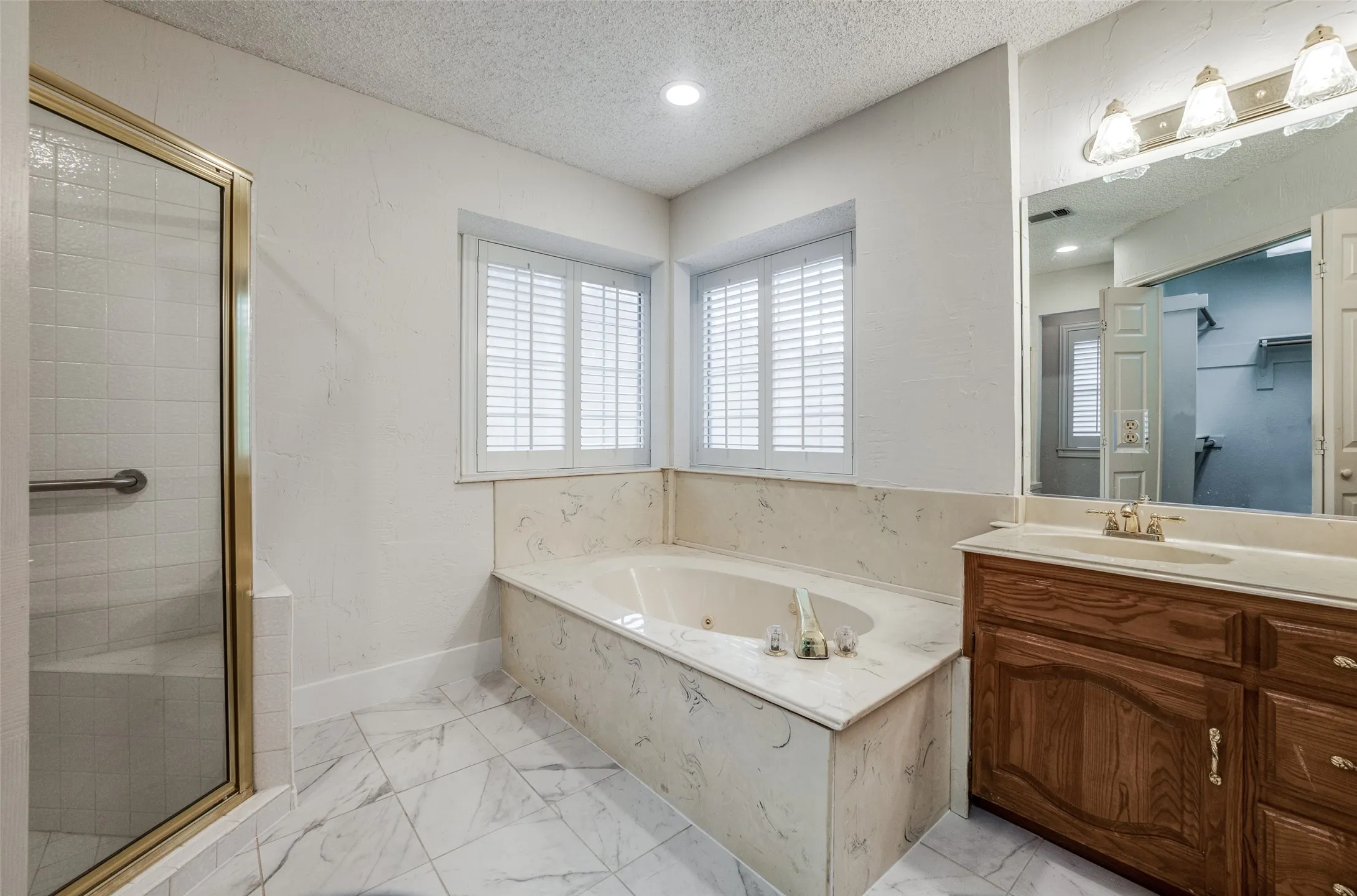 Spa-style bathroom featuring a jetted tub with integrated surround, large vanity with ample storage, and a separate glass-enclosed shower