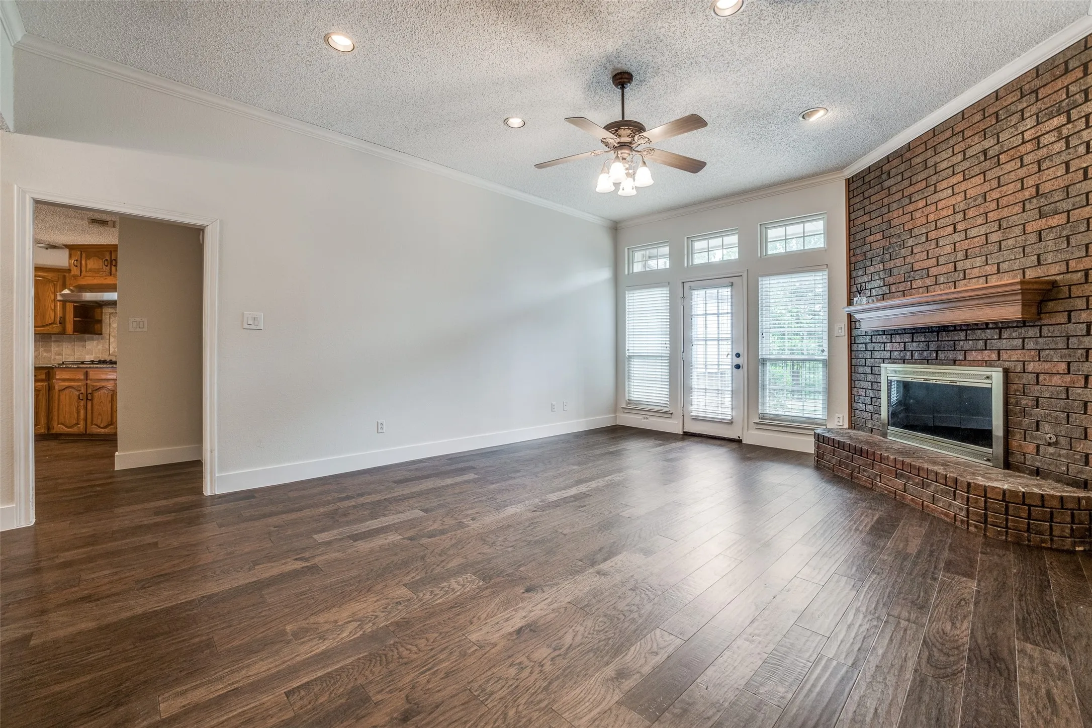 Living area featuring wood-finish flooring, a brick fireplace with a wood mantel, and a ceiling fan with integrated lighting