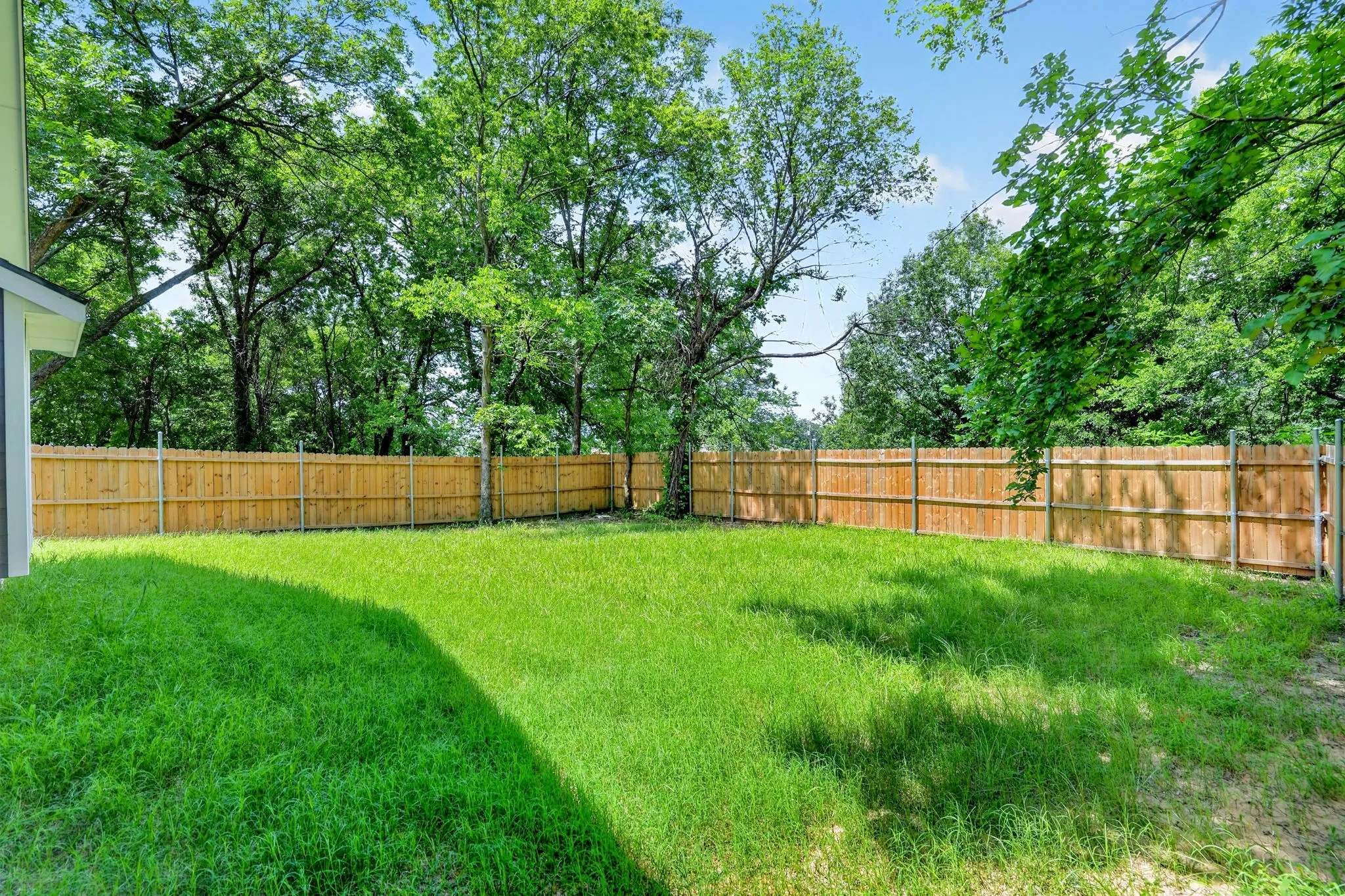 Expansive backyard with a manicured lawn, full privacy fencing, and mature perimeter trees