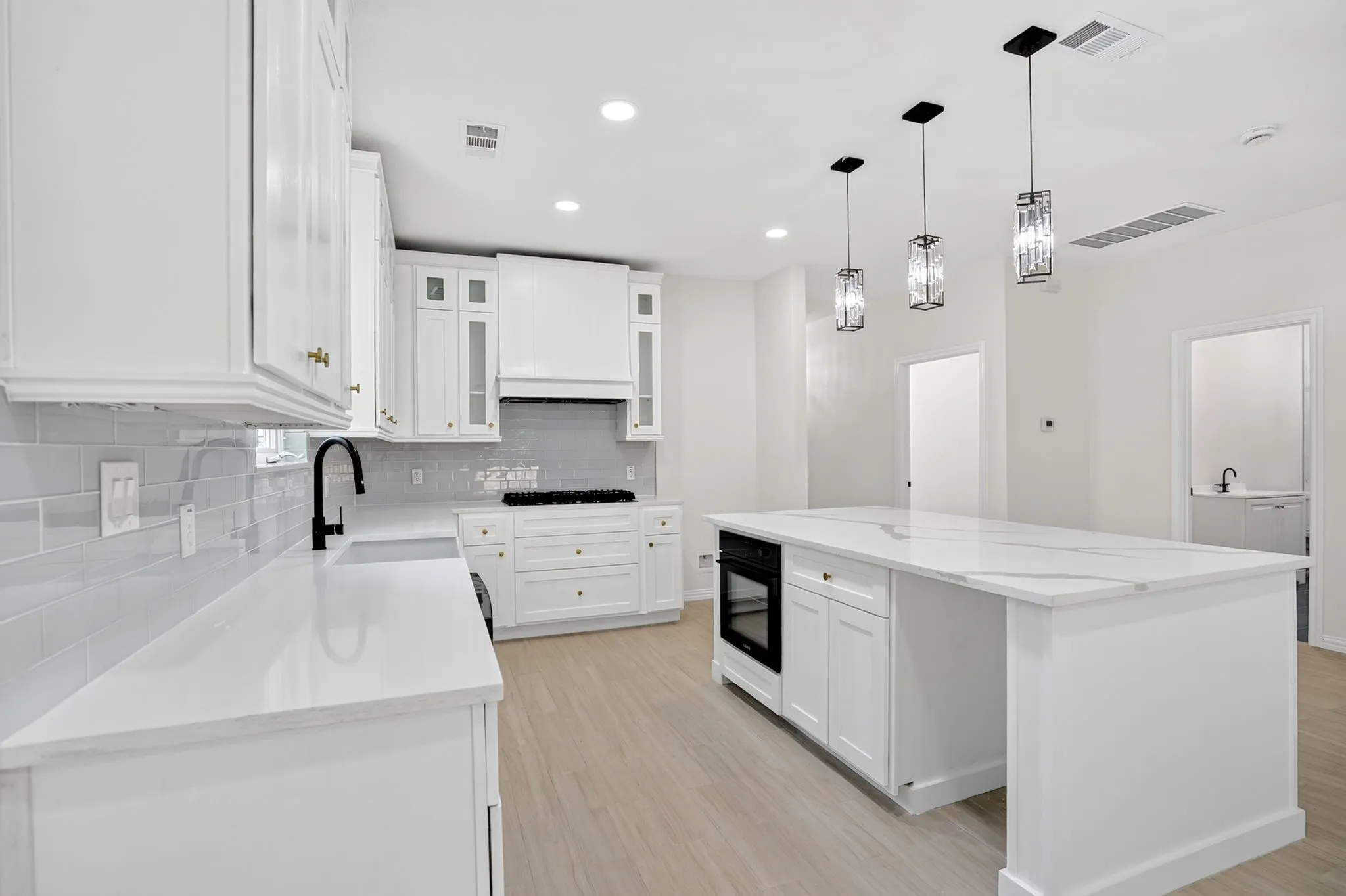 Kitchen featuring an expansive white stone countertop island with an integrated oven and three pendant lights