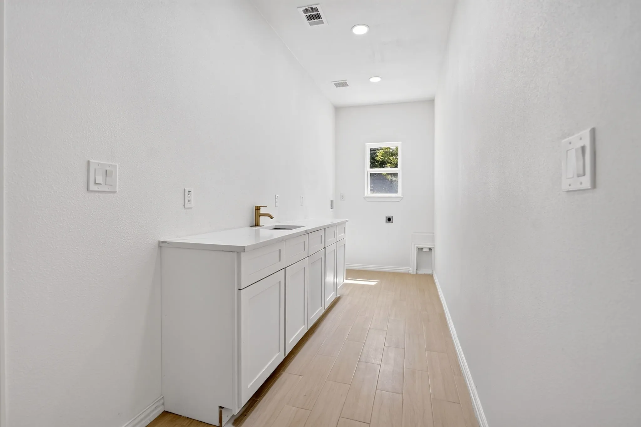 Utility room featuring wood-finish flooring, white cabinetry, a light-toned countertop, and a window for natural light