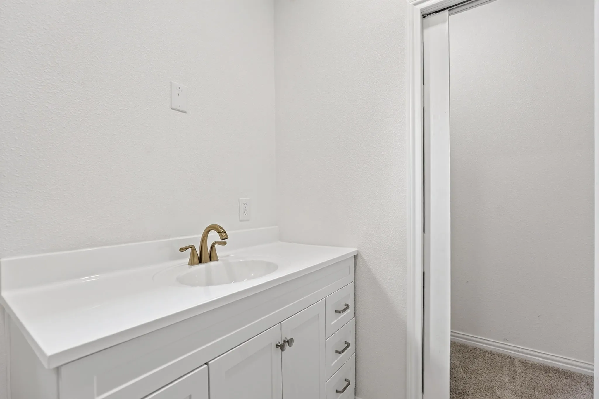 Vanity featuring a white countertop with integrated sink and brass-finish faucet