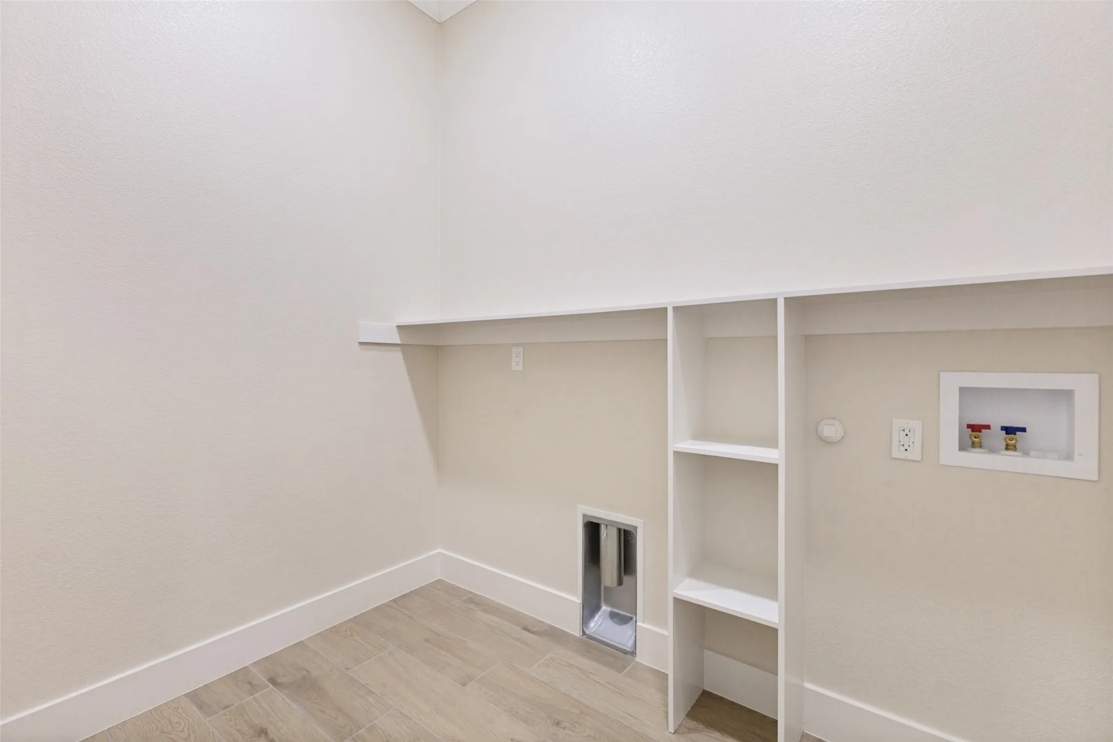 Dedicated utility space featuring built-in shelving, a wall-mounted shelf, a dryer vent, and plumbing hookups