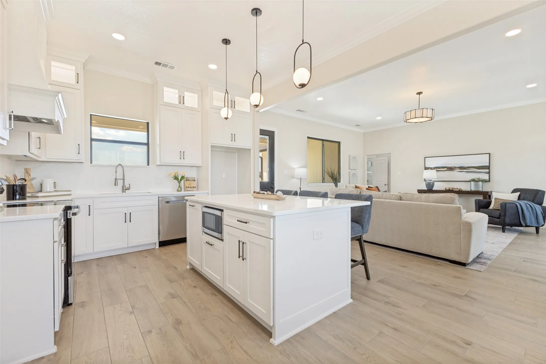Open-concept kitchen featuring an island with built-in microwave, white cabinetry, integrated stainless steel appliances, and wood-finish​​‌​​​​‌​​‌‌​‌‌​​​‌‌​‌​‌​‌​​​‌​​ flooring