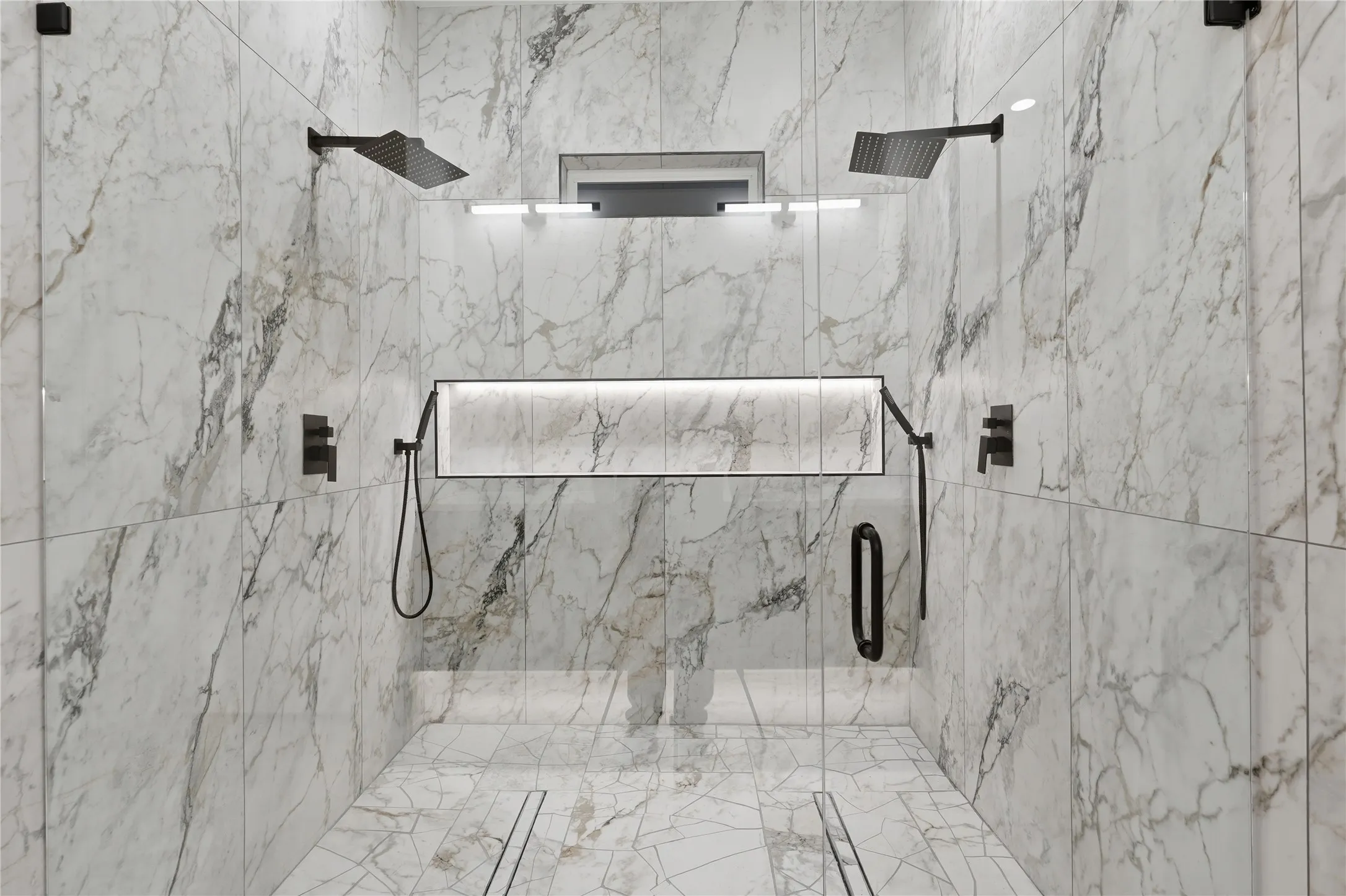 Spacious walk-in shower featuring marble-look wall and floor tiling