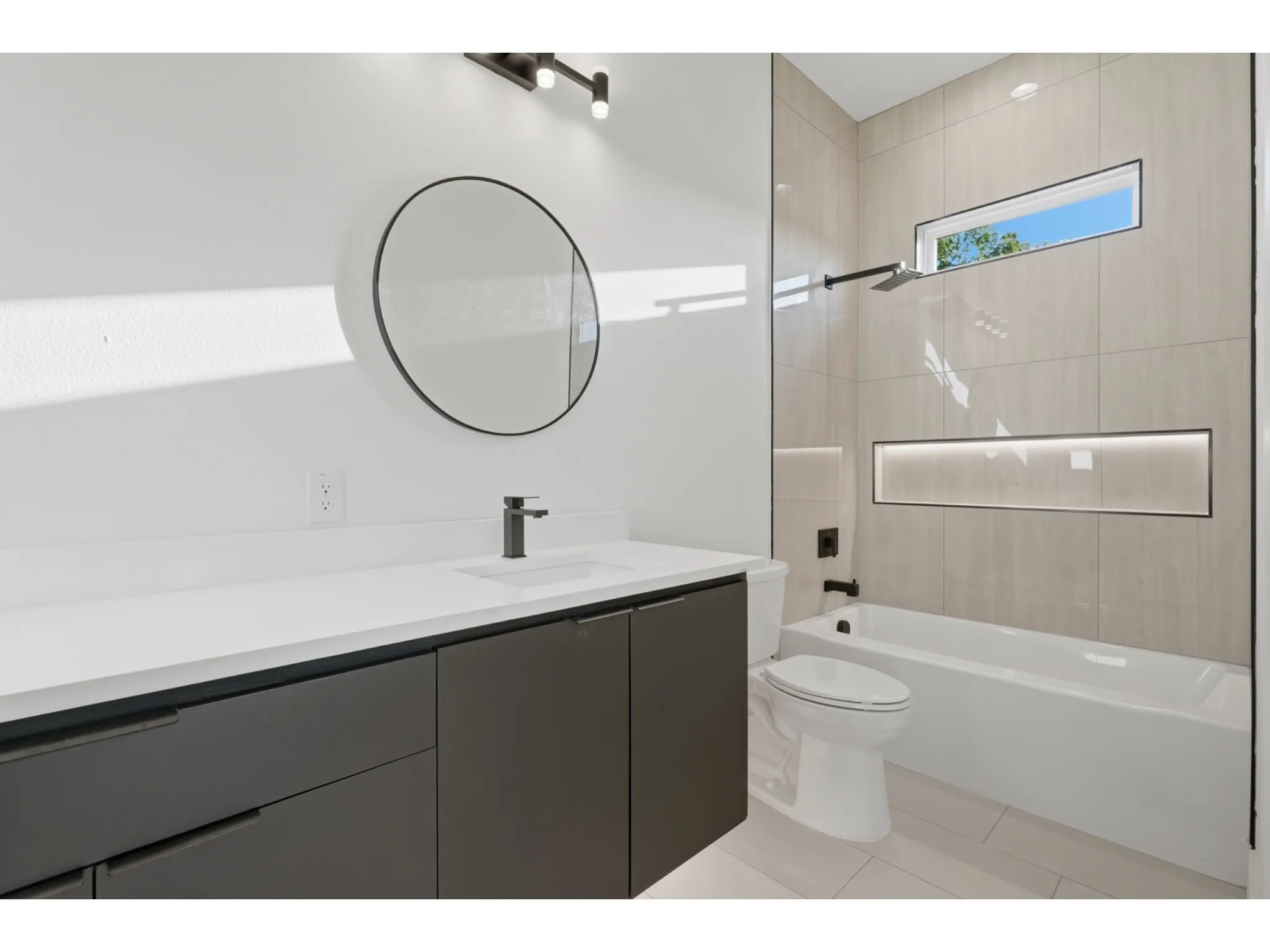 Contemporary bathroom featuring a dark gray floating vanity with a white countertop and a circular mirror