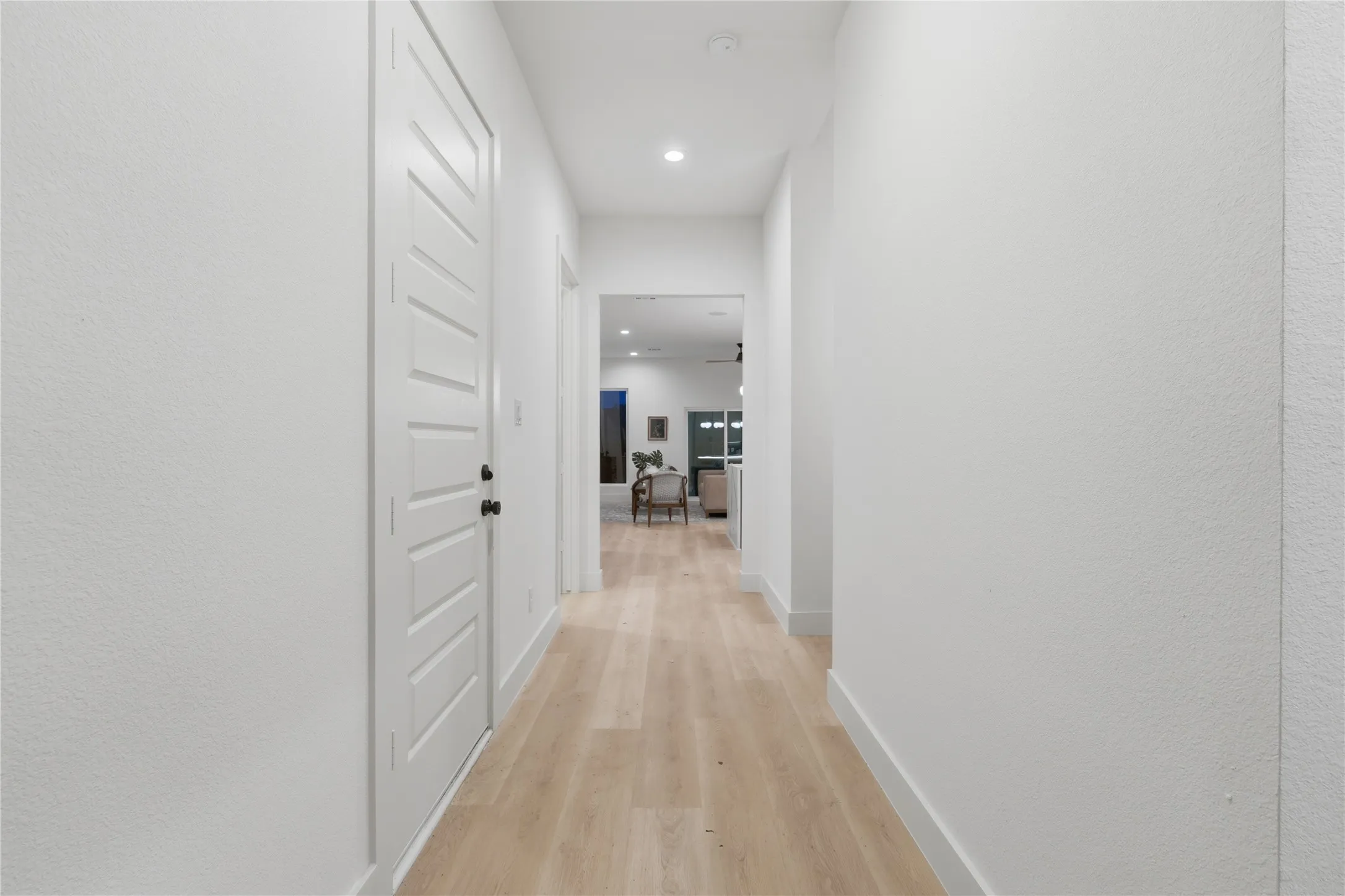 Streamlined hallway featuring light wood-finish flooring, recessed lighting, and crisp white walls