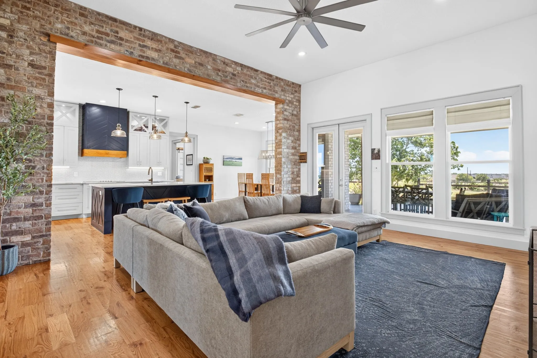 Open-concept living space featuring wood-finish flooring, a contemporary ceiling fan, and large windows