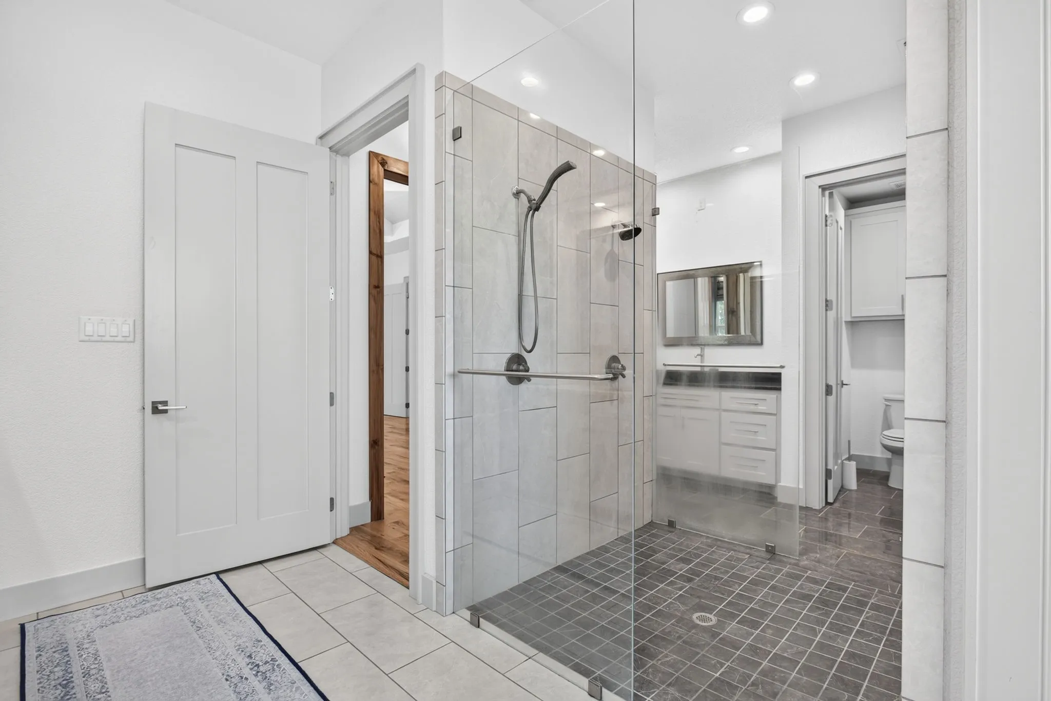 Spacious bathroom featuring a glass-enclosed shower with dual shower heads, light gray subway tile, and a dark gray tiled floor