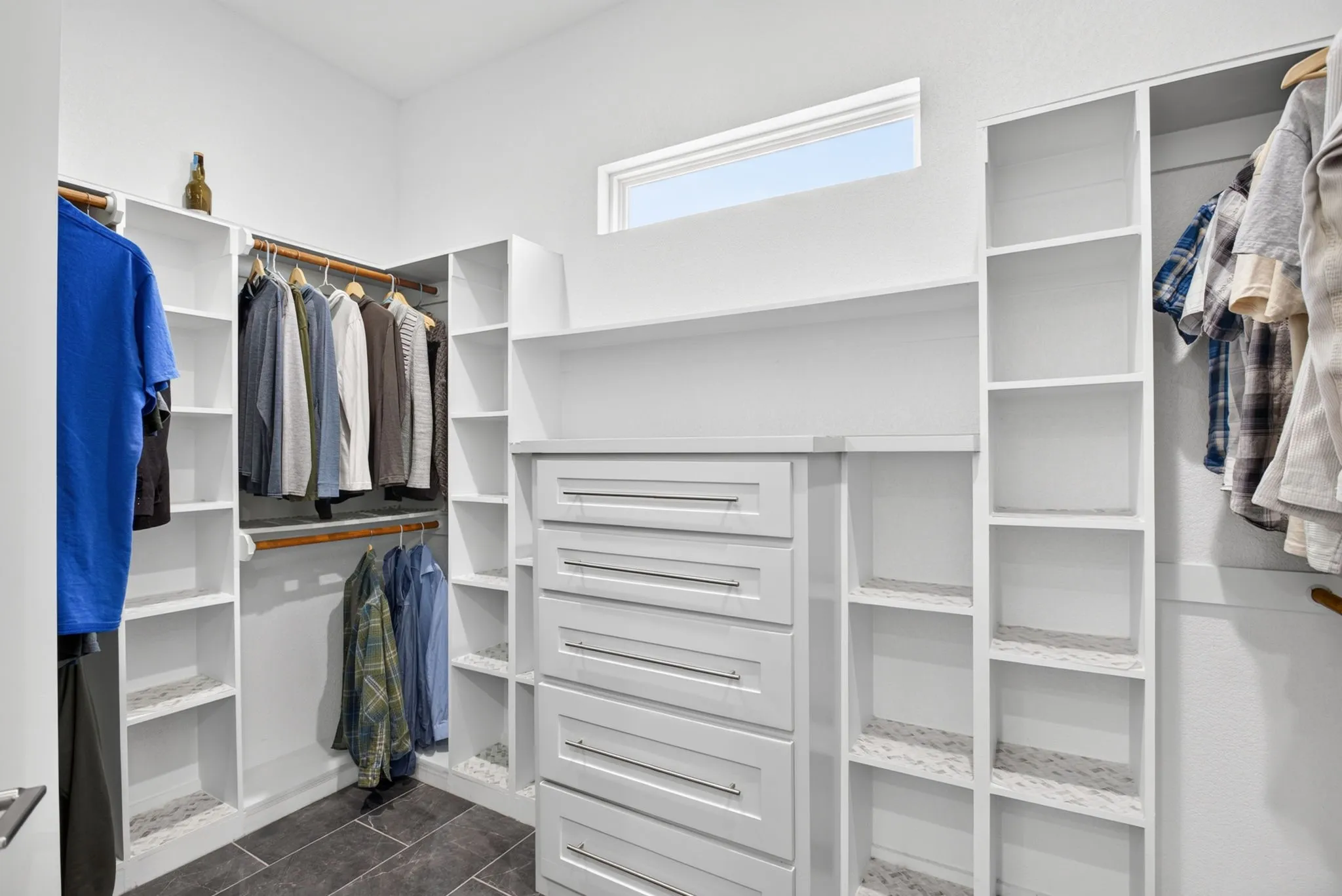 Walk-in closet featuring built-in white cabinetry, multiple shelving units, hanging rods, and an integrated five-drawer dresser