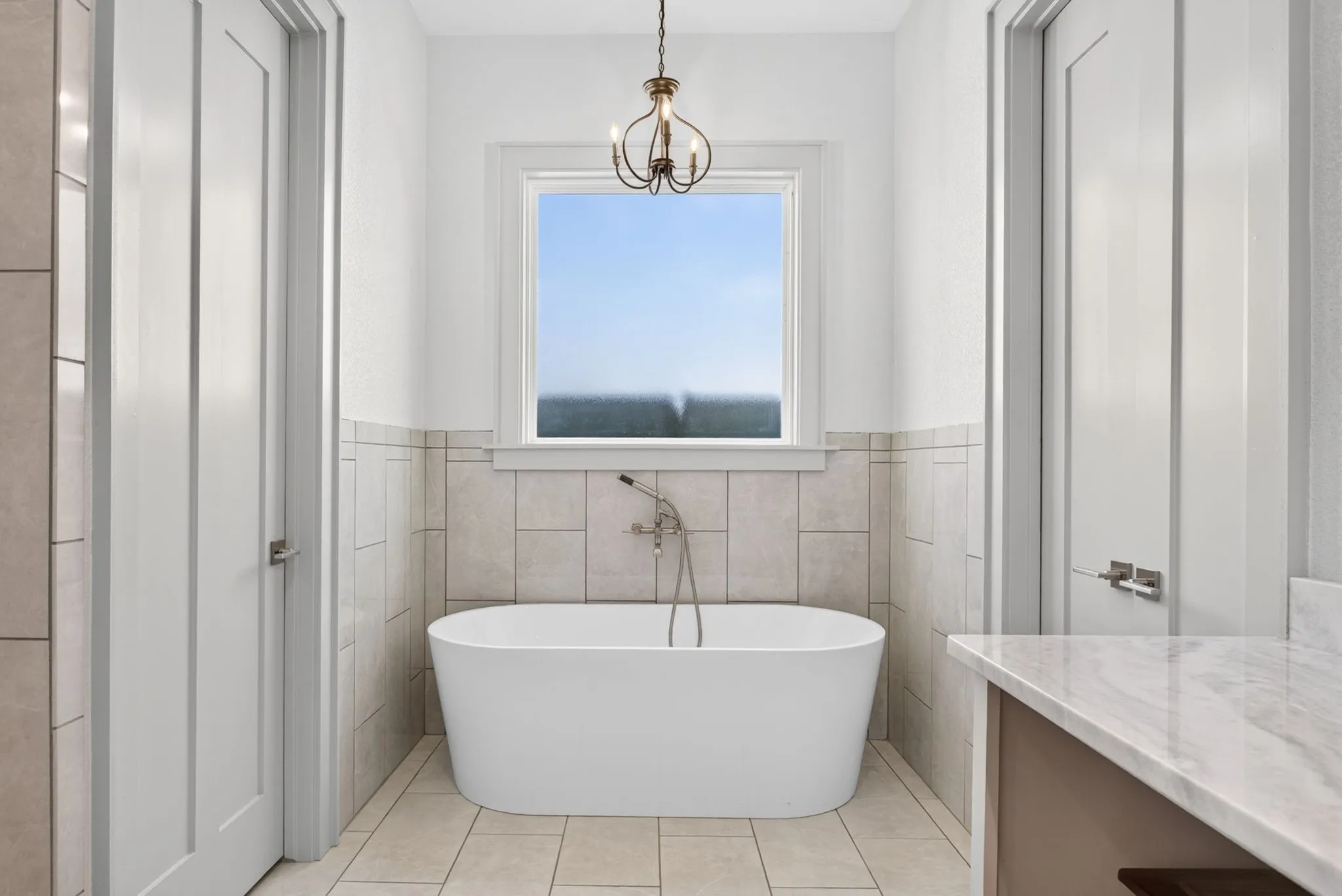 Freestanding soaking tub with a wall-mounted faucet, complemented by a decorative chandelier