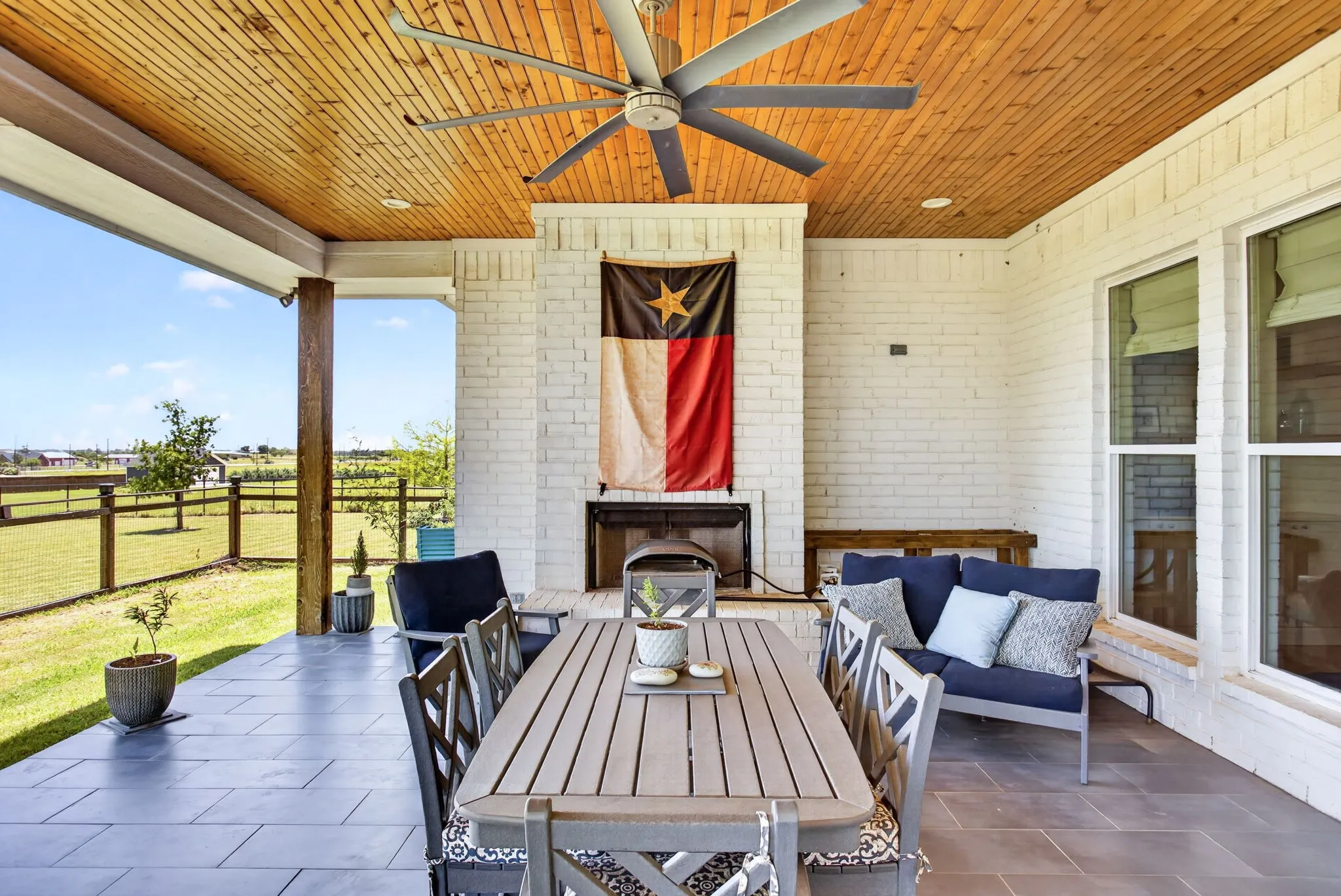Covered outdoor patio featuring a wood-panel ceiling with an integrated ceiling fan, a white brick fireplace, and durable tile flooring
