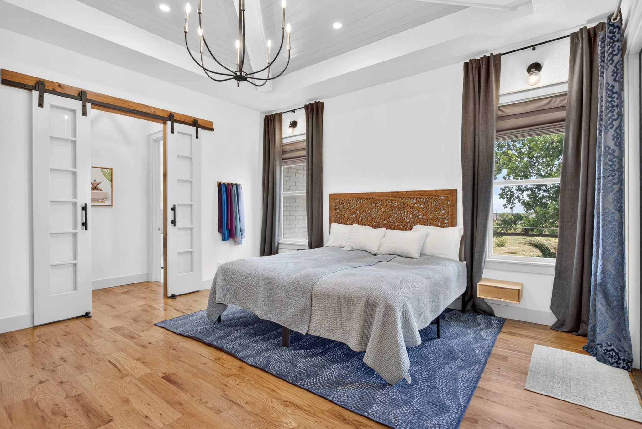 White paneled barn doors with black hardware, wood-finish flooring, and a decorative chandelier