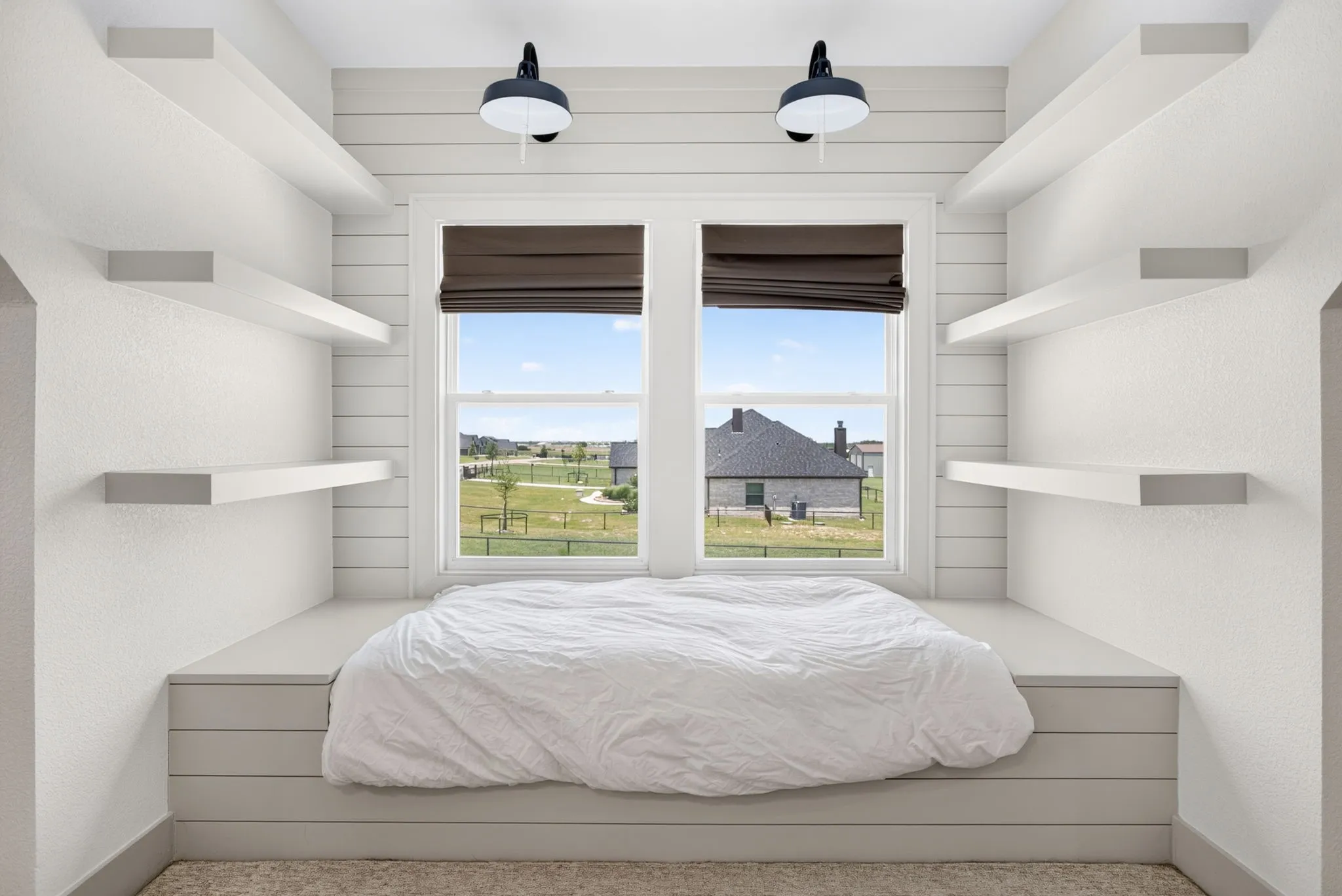 Built-in window bed with shiplap detailing, dual sconce lighting, two windows with Roman shades, and six floating wall shelves