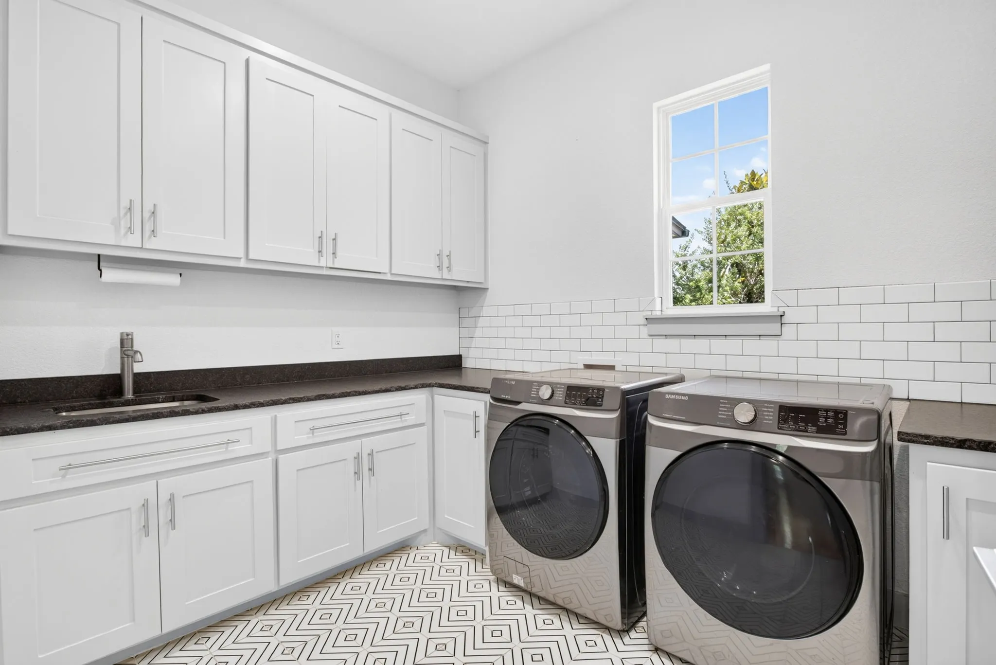 Utility room featuring white shaker cabinetry, dark countertops, a stainless steel sink, and white subway tile backsplash