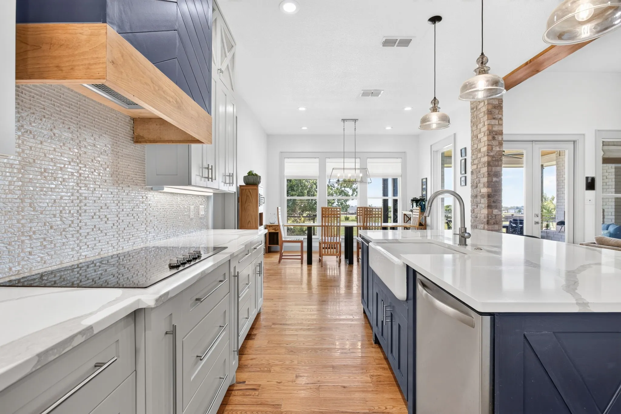 Open-concept kitchen featuring an expansive island with a farmhouse sink, stainless steel appliance, wood-finish flooring, white countertops, and a decorative tile backsplash