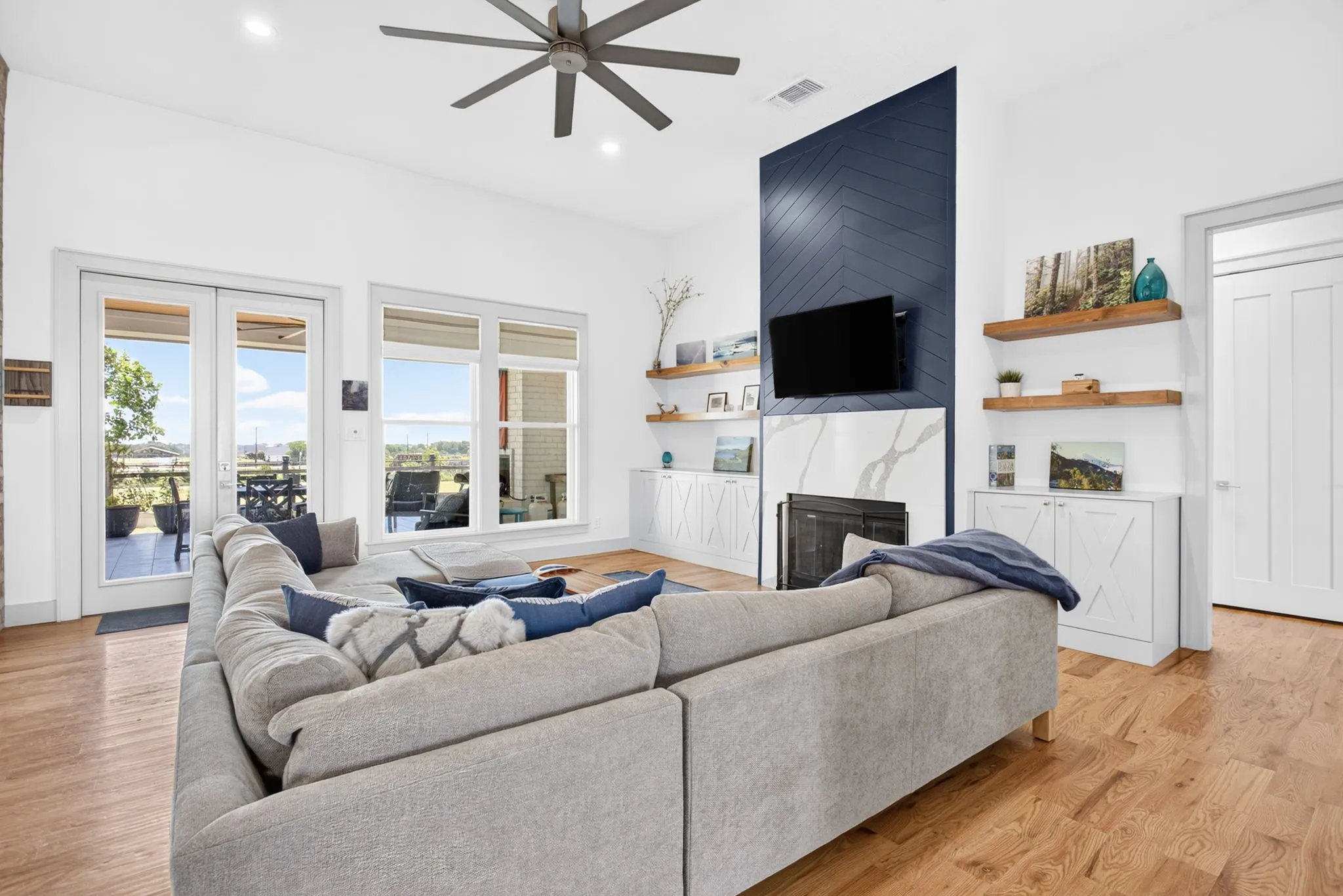 Spacious living area featuring light wood-finish flooring, a contemporary ceiling fan, and a fireplace with a striking blue chevron-patterned accent wall and a light-colored surround