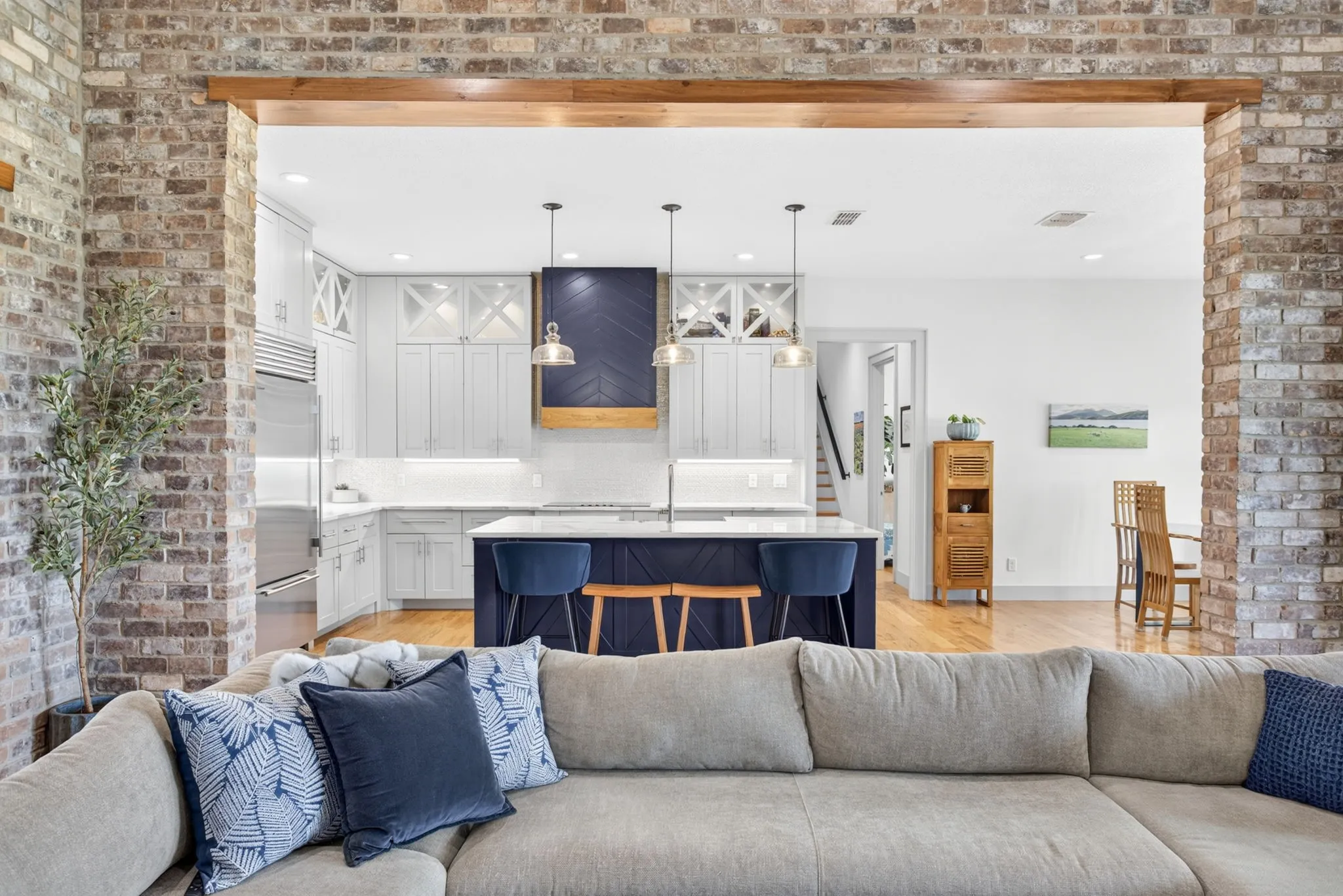 Spacious interior featuring a brick archway and wood beam, hardwood flooring, and a modern kitchen with a large island, white cabinetry, and stainless steel appliances