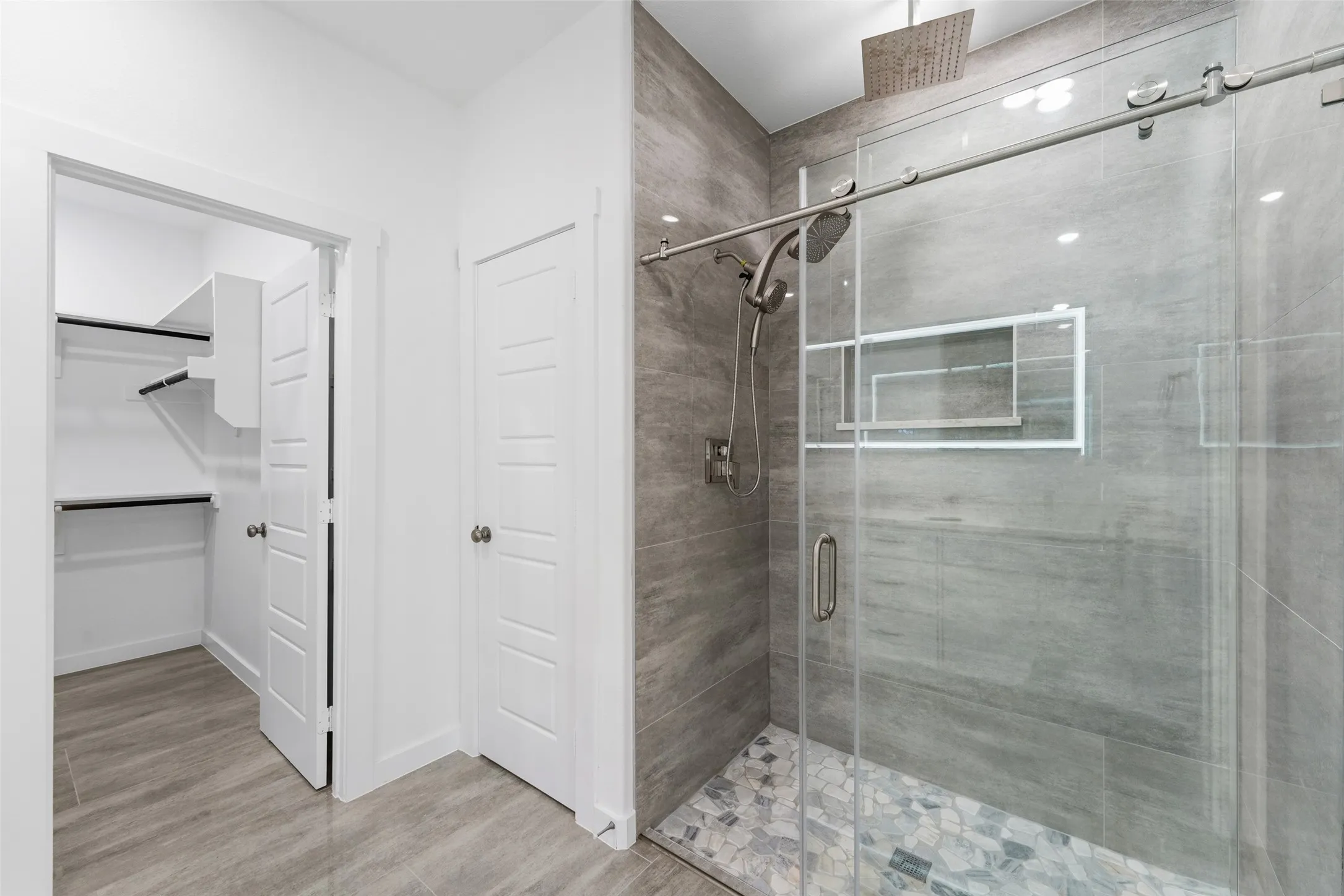 Shower with frameless glass enclosure, rain shower head, hand-held shower, tiled walls, and mosaic tile flooring