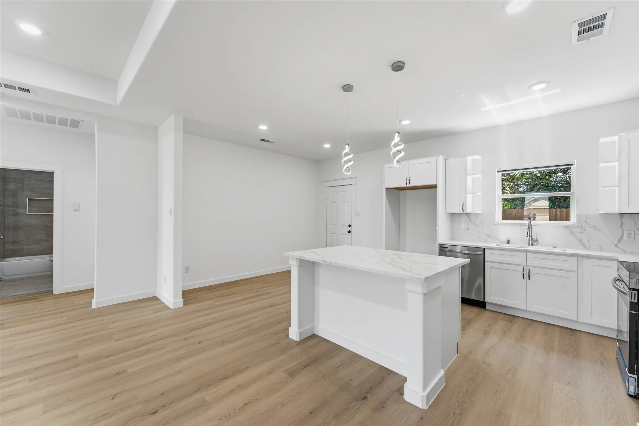Contemporary kitchen featuring a central island with a stone-finish countertop, white cabinetry, stainless steel dishwasher, and designer pendant lighting