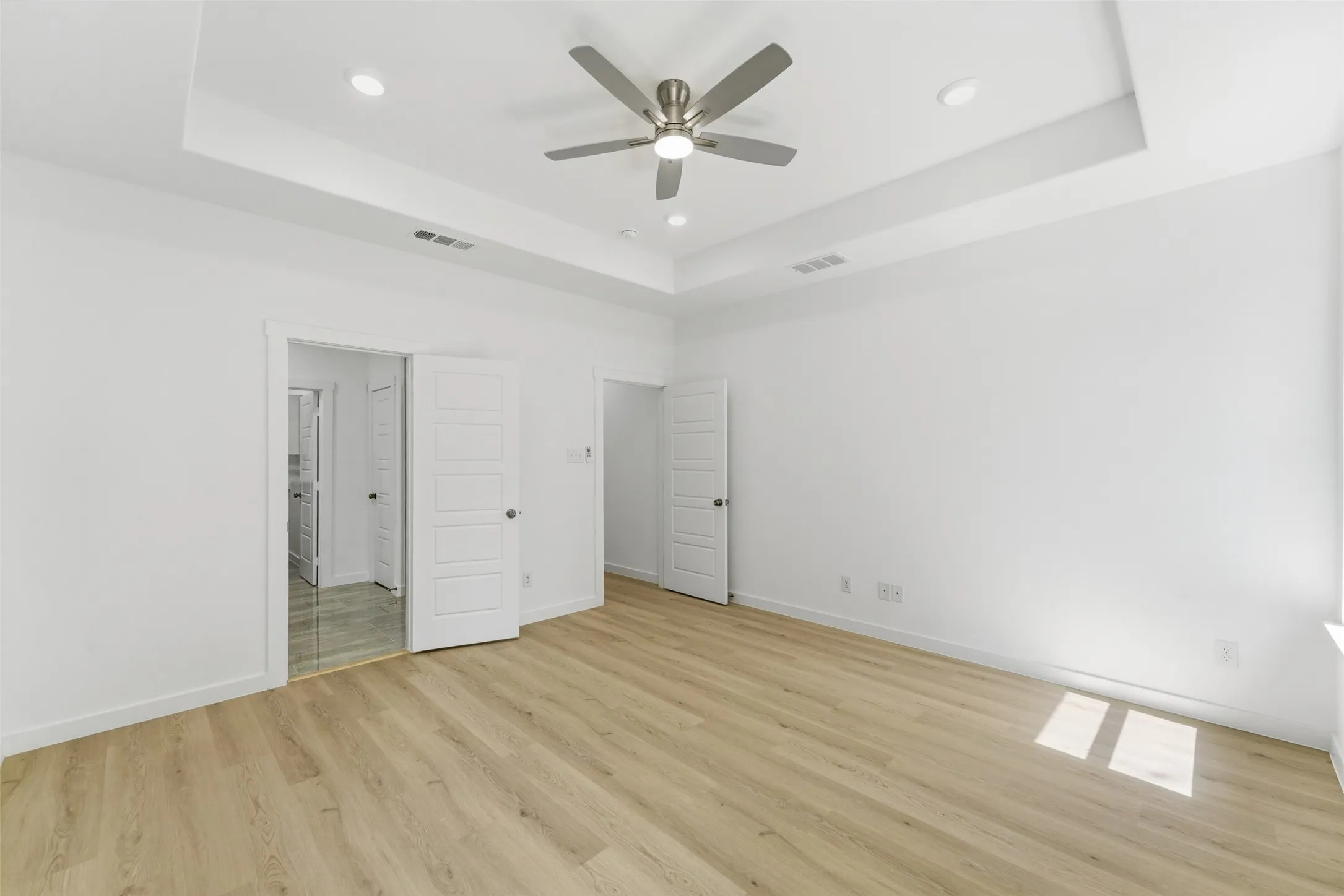 Recessed lighting illuminates a tray ceiling with a brushed nickel ceiling fan