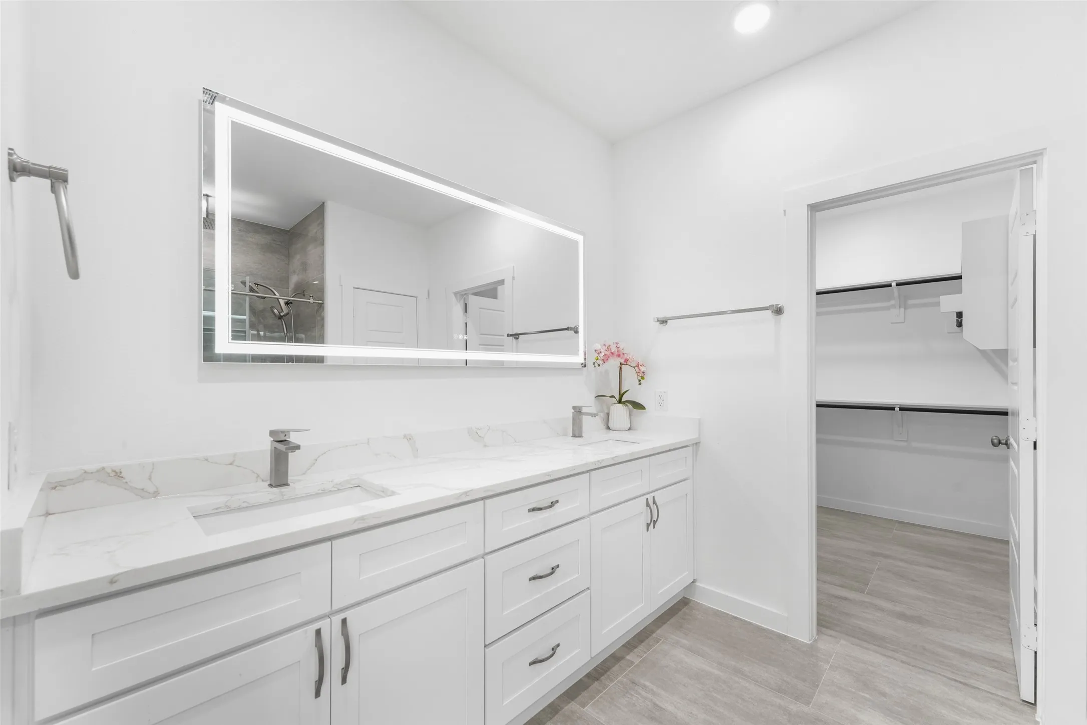 Dual vanity with integrated sinks and white cabinetry, complemented by a large back-lit mirror