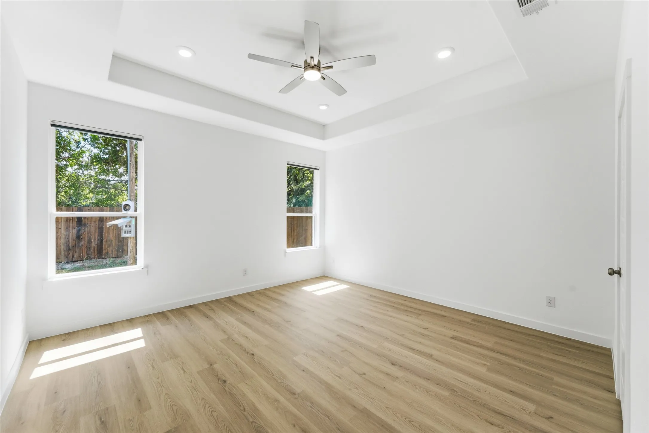 Spacious room featuring wood-finish flooring, a tray ceiling with recessed lighting, and a ceiling fan with integrated lighting