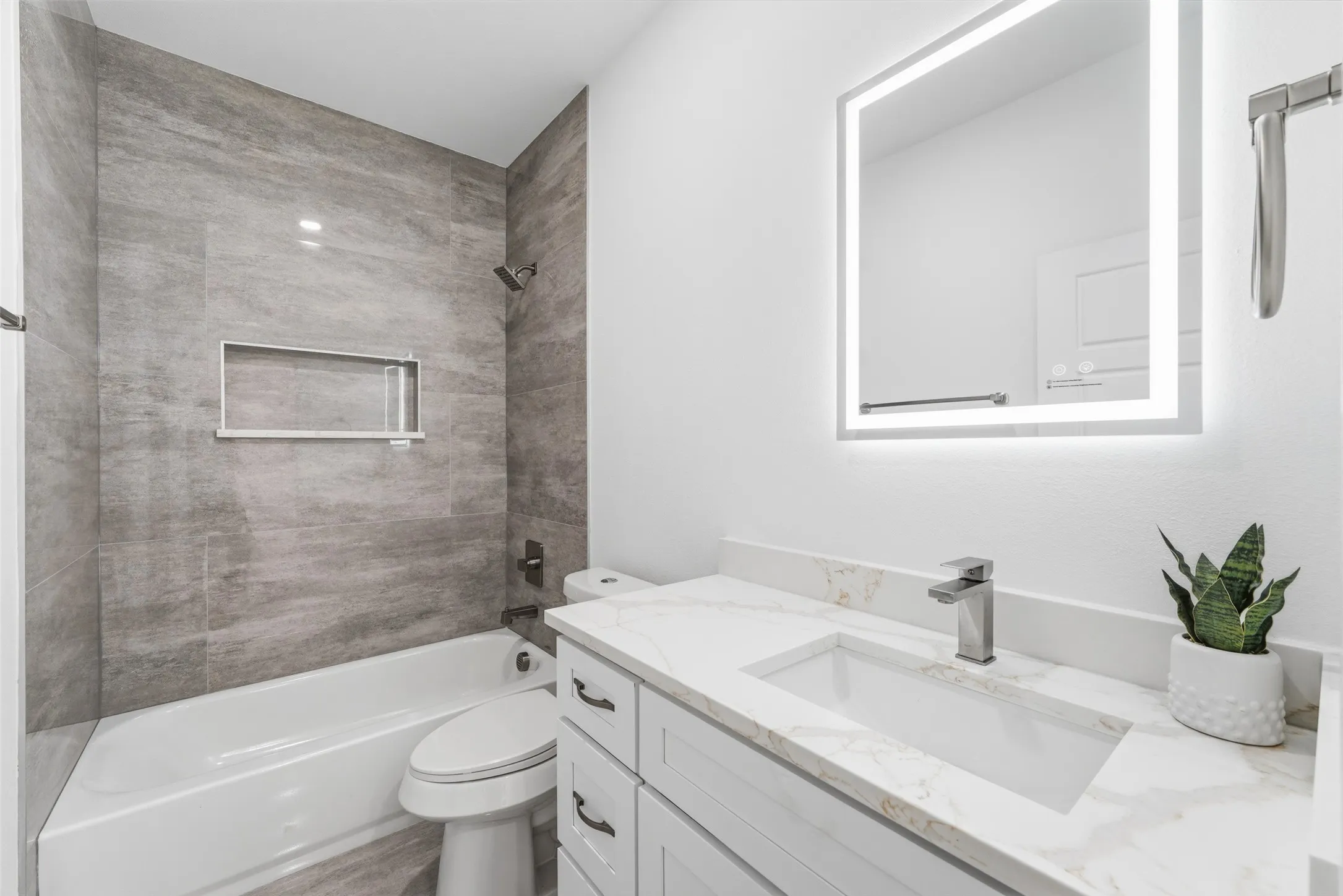 Bathroom featuring a tub/shower combination with gray tile surround and a built-in niche