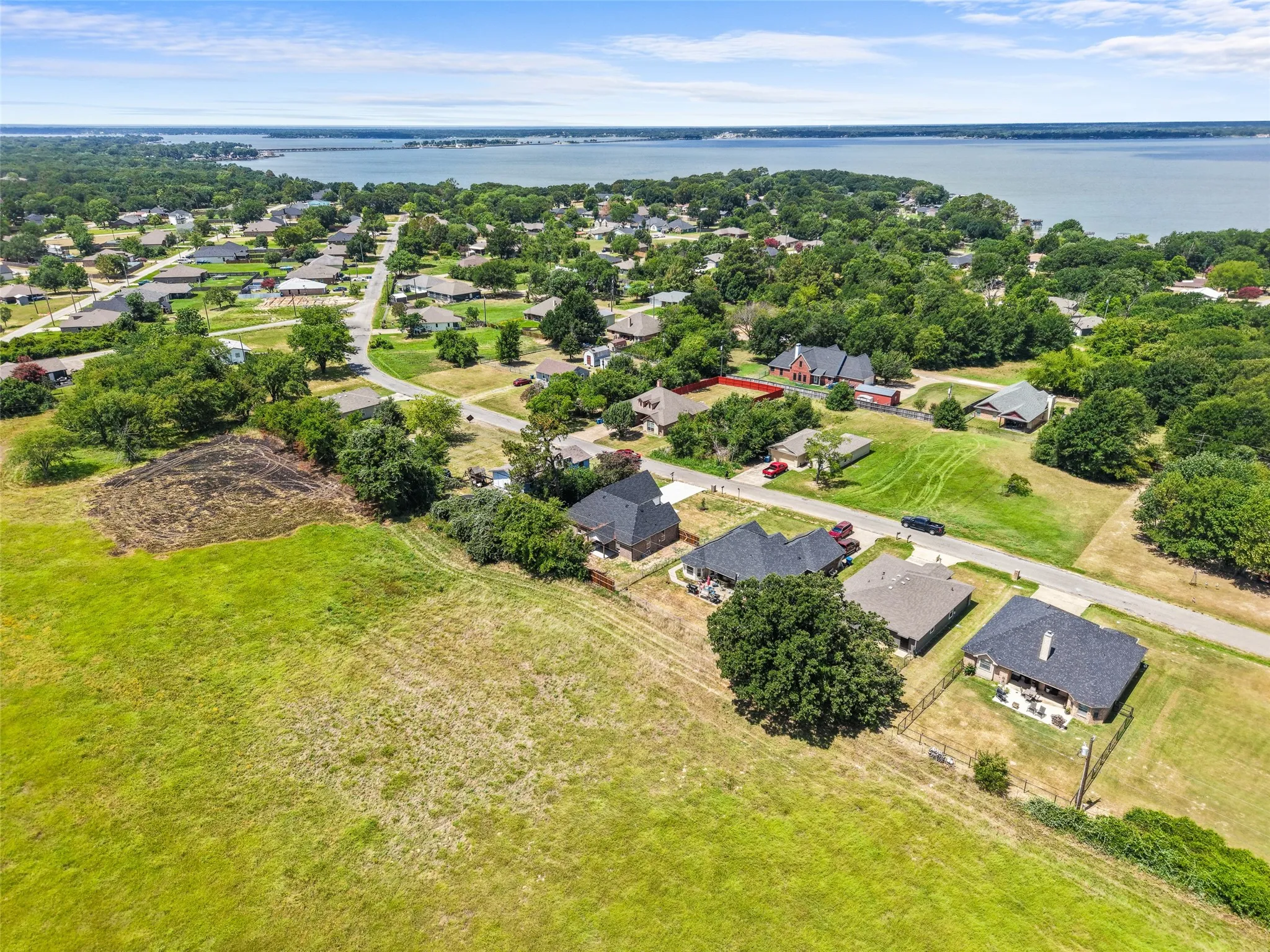 Aerial perspective featuring a residential area with varied housing styles, mature trees, and a distant body of water