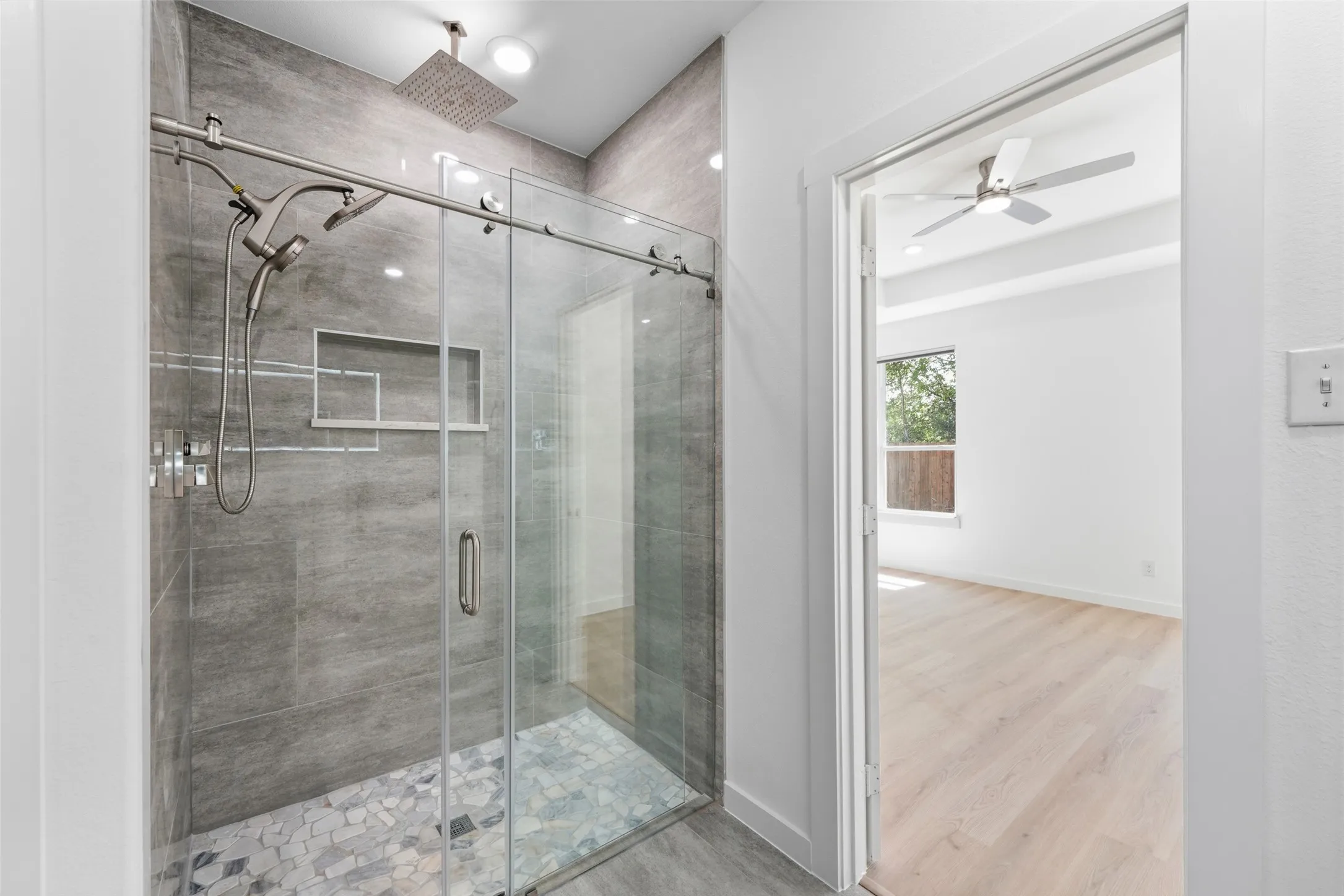 Modern glass-enclosed shower with a rainfall showerhead, handheld sprayer, and tiled walls