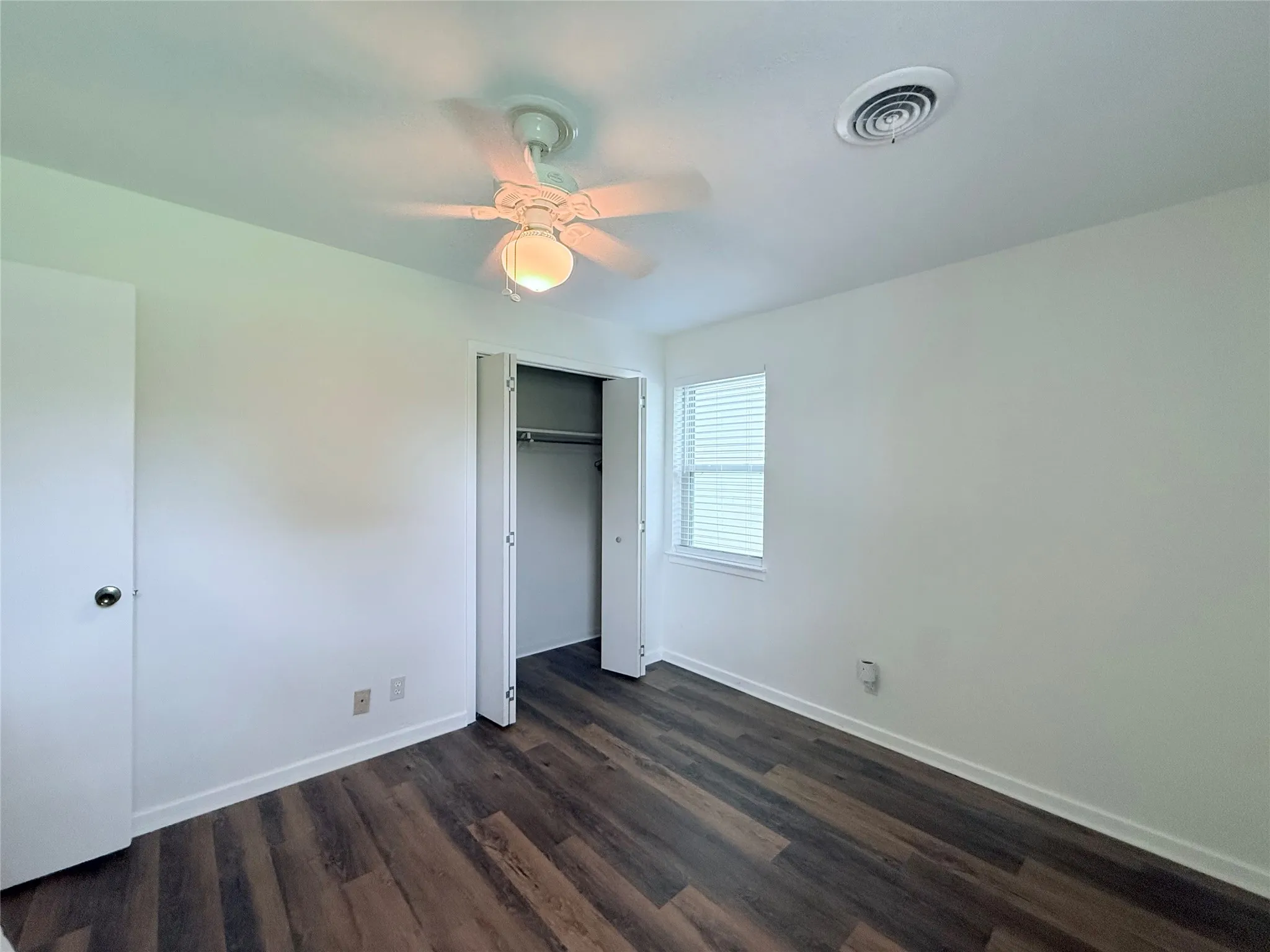 Room featuring wood-finish flooring, white walls, and a ceiling fan with integrated lighting